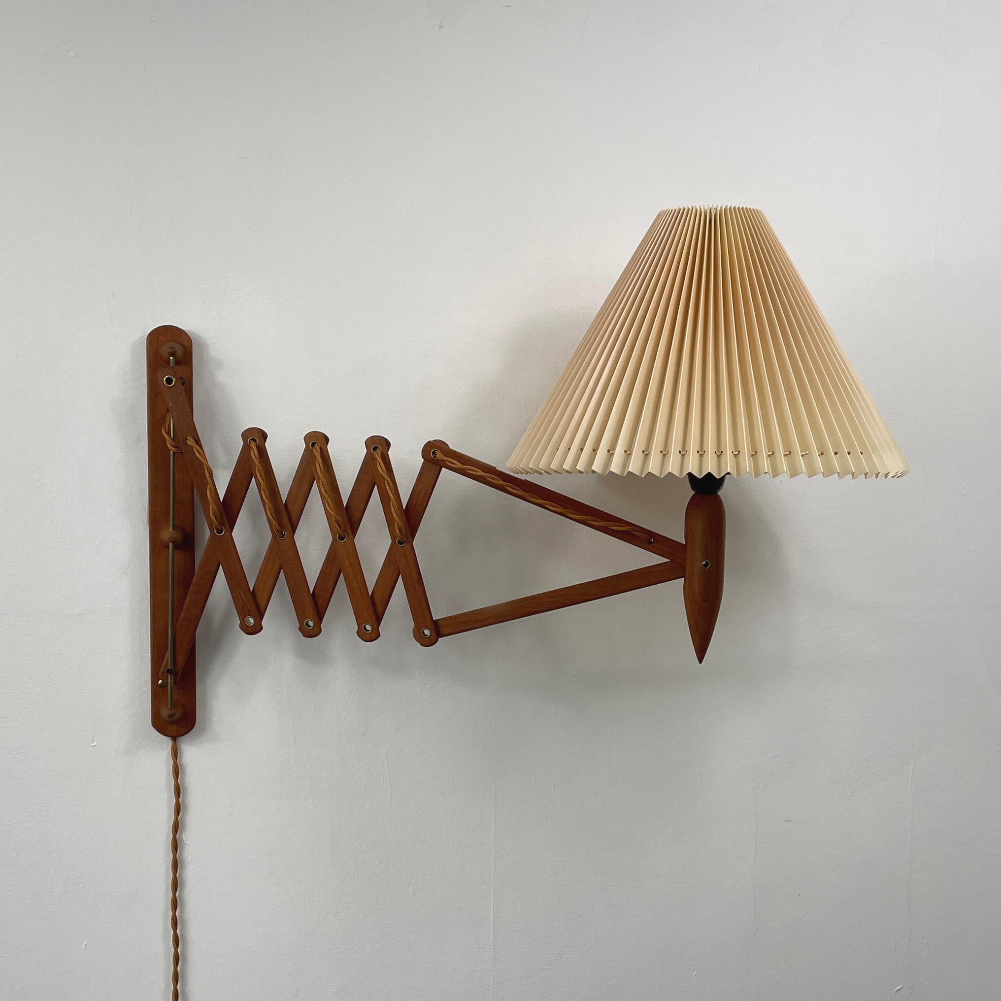This beautiful wall light was designed by Kaare Klint and manufactured in Denmark in the 1950s. It features a teak scissor adjustable lamp arm and a pleated cream colored – also adjustable – plastic lampshade. The lampshade is original. 

The light
