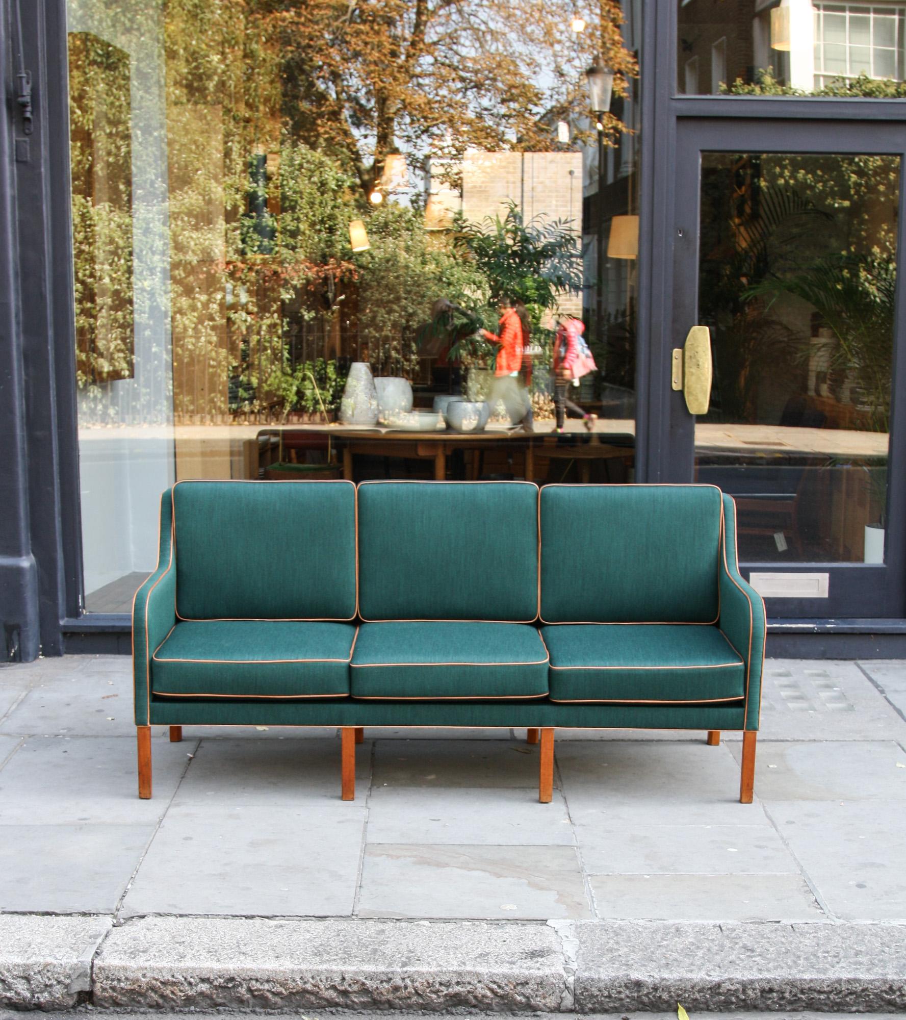 A vintage three-seat sofa by Kaare Klint, Denmark, 1940s. Reupholstered in a radiant green fabric with cognac leather trim, the sofa stands on eight solid mahogany legs and has six copper springs coiled cushions, which confers the sturdiness and