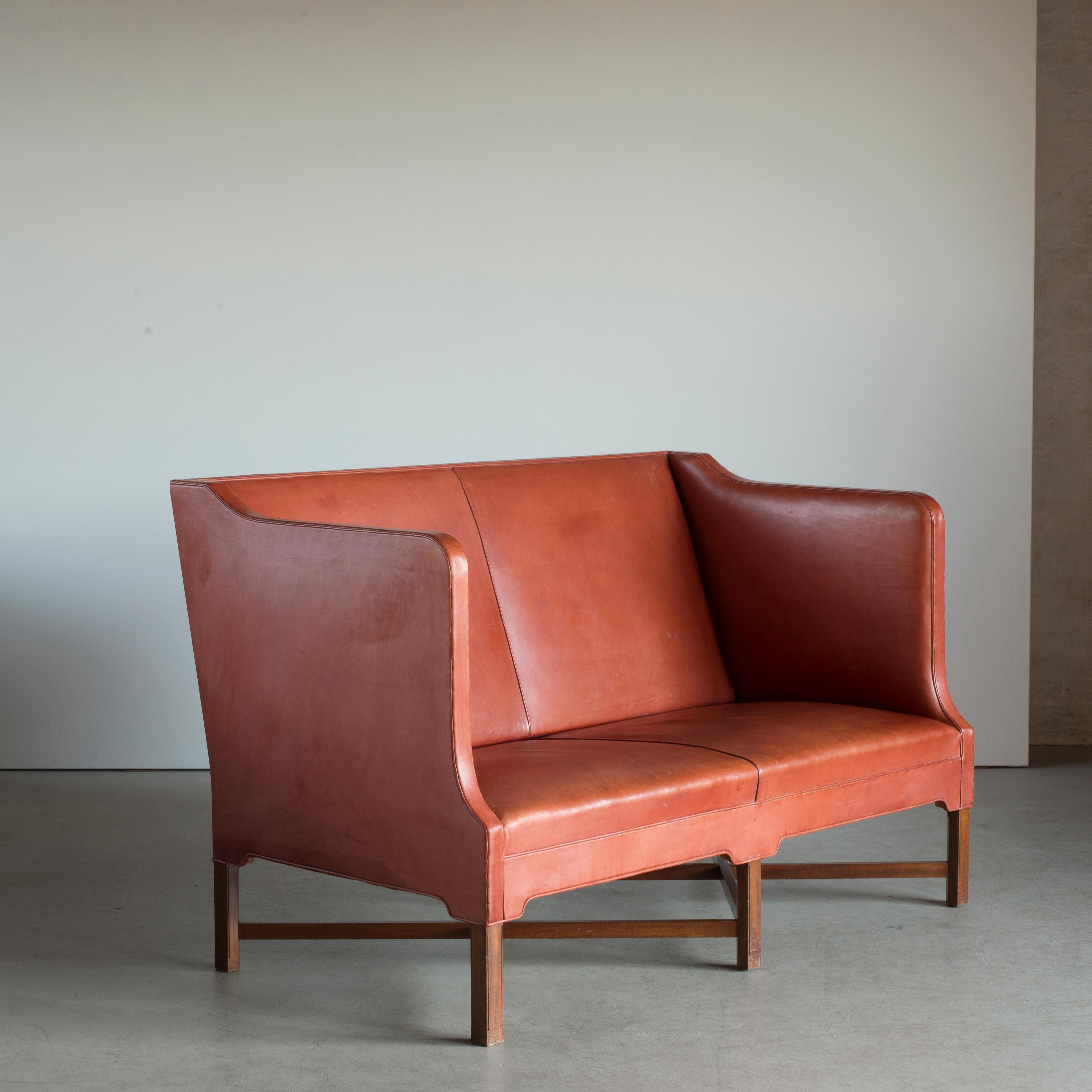 Kaare Klint freestanding two-seat sofa on six-legged, profiled mahogany cross-frame. Sides, seat and back upholstered with patinated leather. Executed by Rud. Rasmussen, Copenhagen.

Reverse with paper labels ‘RUD.