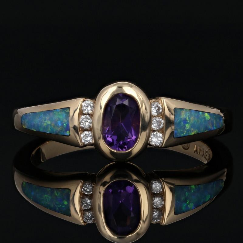Pure enchantment! Fashioned in classic 14k yellow gold, this beautiful NEW Kabana ring features a royal-purple amethyst solitaire bordered in crescents of diamonds. Inlaid opals add flames of blue-green fire to the sides of the band as they merge