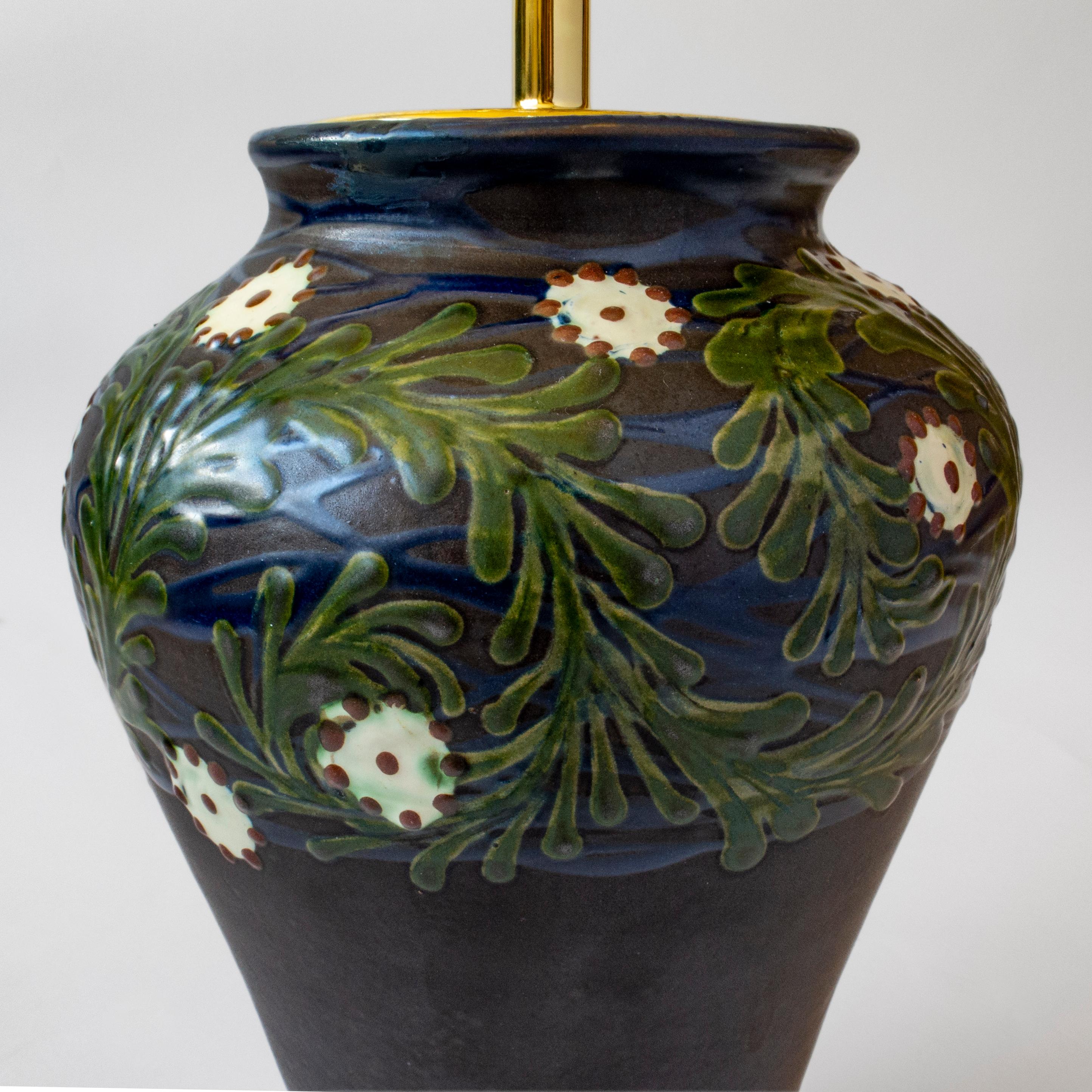 Die spitz zulaufende, hochschulterige Vase ist mit weißen und purpurroten Blüten geschmückt, die in wirbelnde, bunte, grüne Wedel und ultramarinblaue Wellen eingebettet sind, die auf dunkelblauem Grund stehen und in einem kannelierten, weiß
