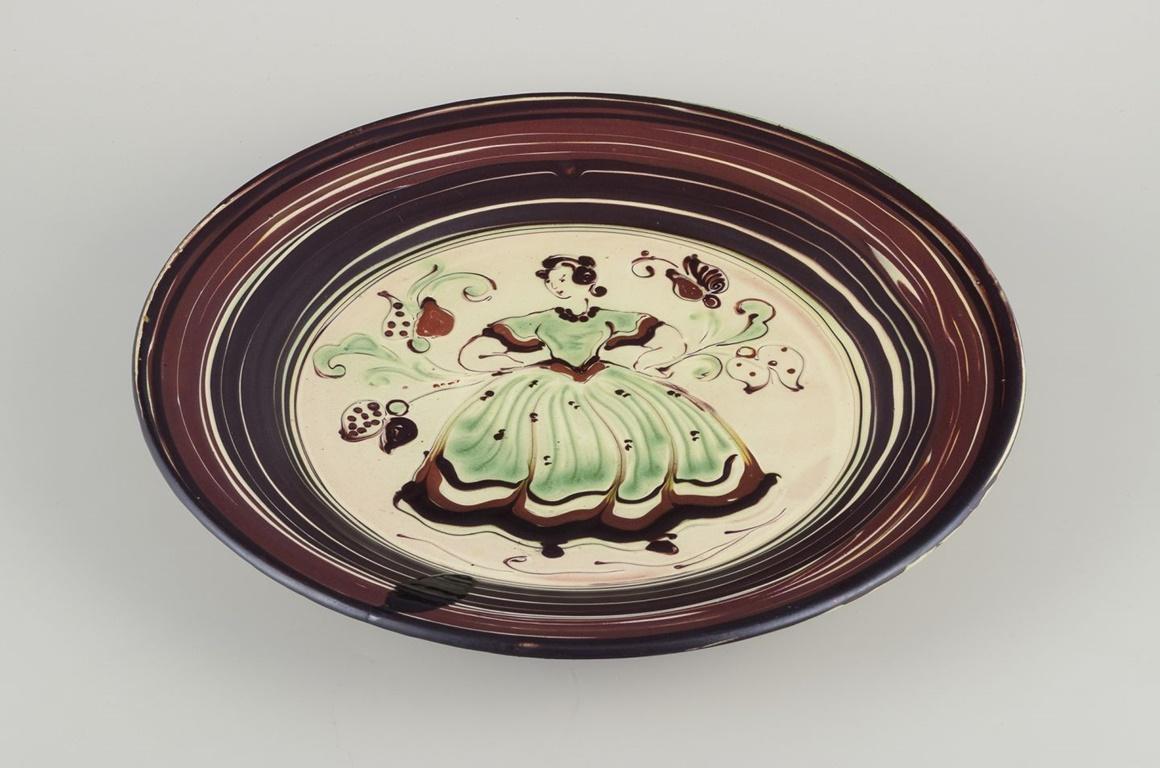 Pre-owned goods are exempt from import duties for U.S. customers. 
Therefore, no import tariffs will be applicable to your purchase.

Kähler, Denmark.
Large ceramic dish with a motif of a dancing woman.
Polychrome glaze. Hand-glazed.
With a hanging