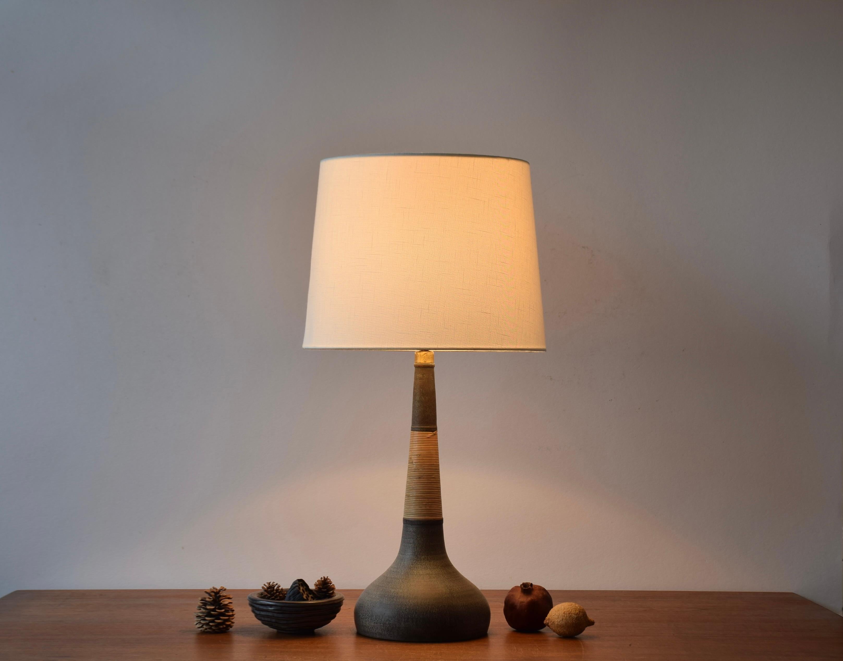 Lampada da tavolo alta in ceramica realizzata dal laboratorio di ceramica danese Kähler (HAK) in collaborazione con il produttore di paralumi danese Le Klint. 

La lampada è realizzata in ceramica non smaltata avvolta da una canna intorno al collo e