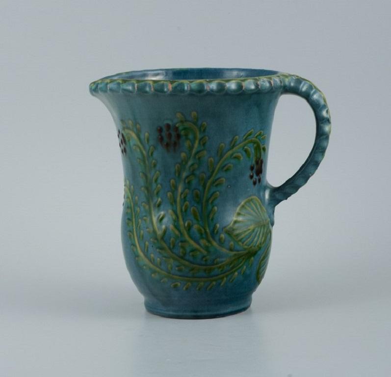 Kähler jug ??in glazed ceramic. 
Decorated with flowers on a blue background.
1930s/40s.
In great condition.
Signed.
Measurements: H 18.5 x D (incl. handle) 18.0 cm.
 