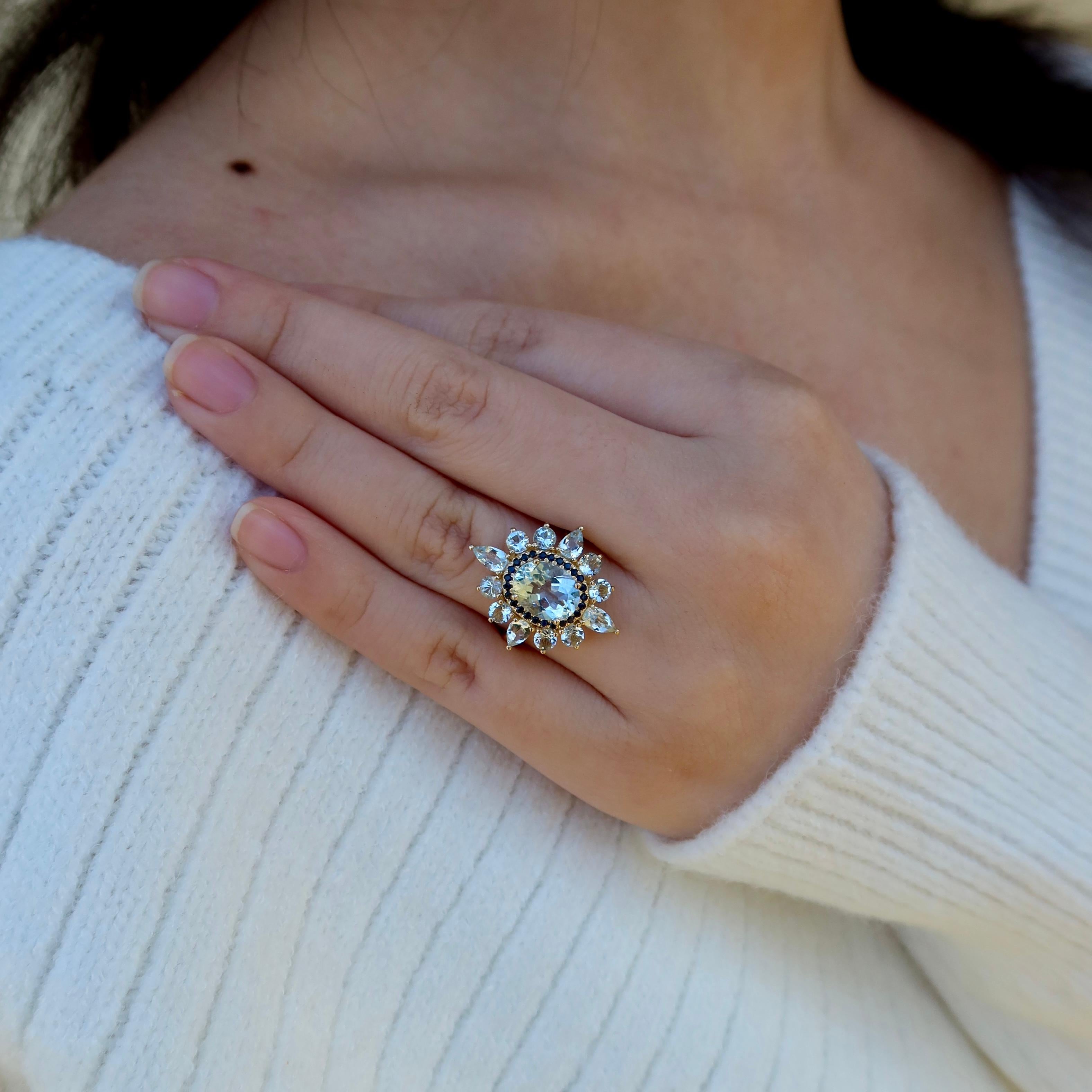 A striking blend of color and brilliance, this Kai Aquamarine Sapphire Cocktail Ring is designed to turn heads. At the center, a glowing oval aquamarine catches the light with its soft, icy blue hue, surrounded by a halo of deep blue sapphires that