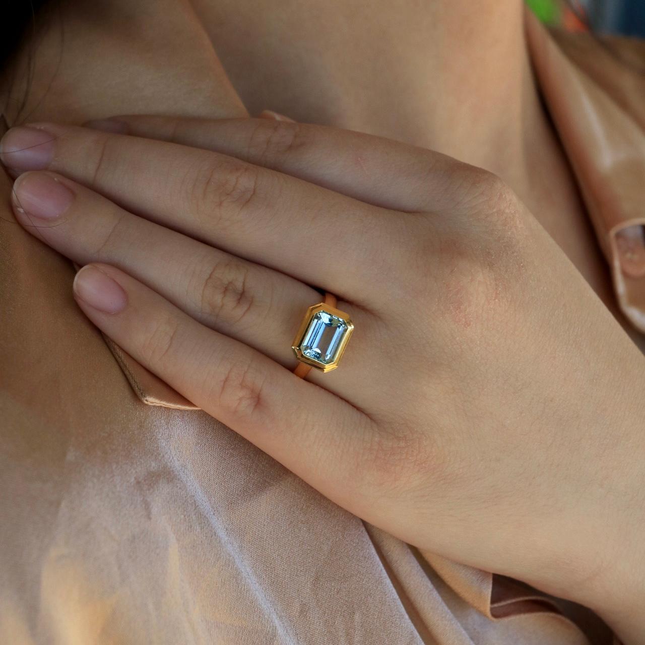 At its heart lies a mesmerizing east-west emerald-cut 2.2 ctw aquamarine, radiating serene hues reminiscent of clear skies and tranquil seas. The horizontal setting breathes fresh life into the classic gemstone, offering a contemporary twist to a