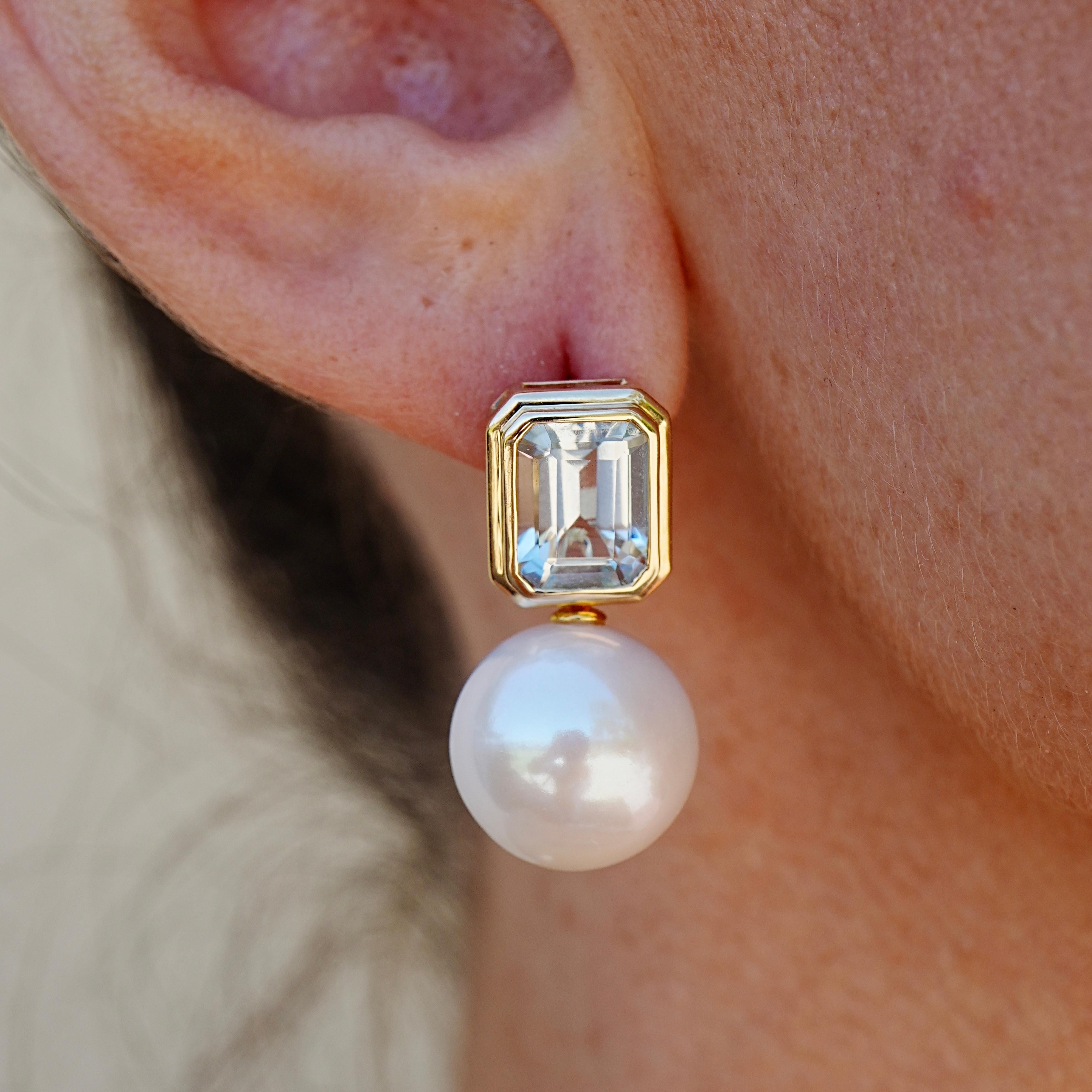 Kühle Klarheit trifft auf organische Weichheit in diesem eleganten Cabrio-Design. An der Spitze glänzt ein Paar Aquamarine im Smaragdschliff mit eisiger Präzision, eingefasst in 14 Karat Gelbgold, um jede Facette hervorzuheben. Unten sorgen
