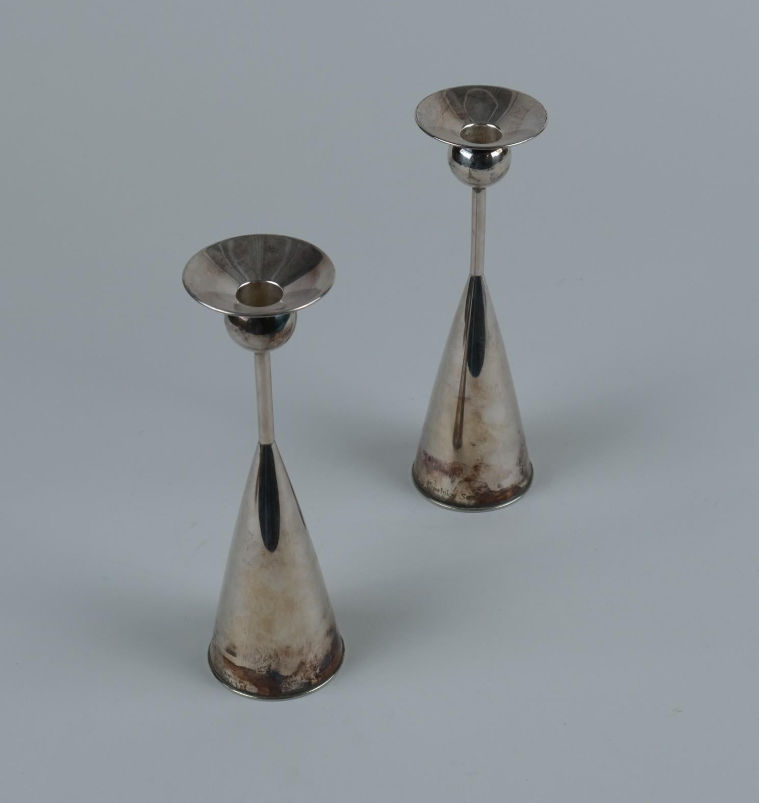 Coppia di eleganti portacandele disegnati da Kai Blomqvist e prodotti da Kultakeskus Oy nel 1965. Entrambi i pezzi presentano una serie di marchi e timbri che indicano che si tratta di argento massiccio, prodotto da Kultakeskus Oy, e in base al