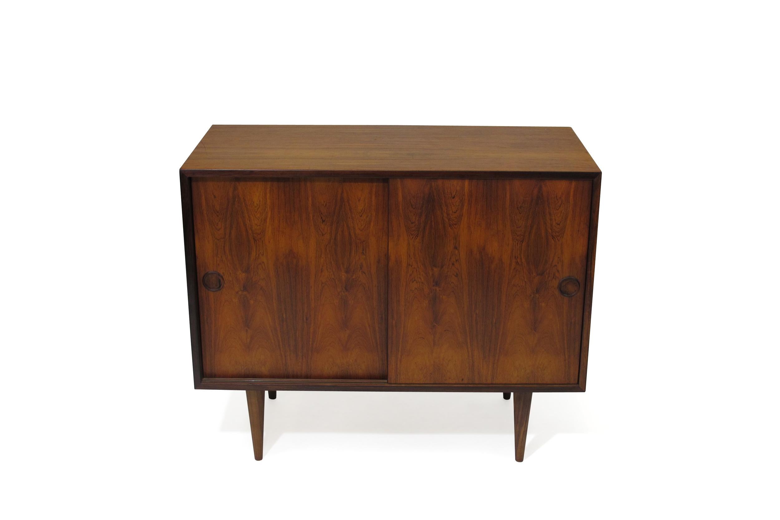 Rosewood cabinet designed by Kai Kristiansen with book-matched sliding doors, revealing a mahogany interior with an adjustable shelf and silverware drawer. Minimal design with lovely details such as mitered corners and hand-carved inset pulls. Can