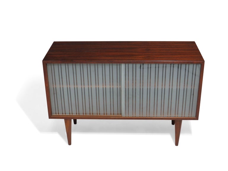 Mid-Century Modern rosewood cabinet designed by Kai Kristiansen and manufactured in Denmark. Crafted of rosewood with adjustable shelves on both sides, and two frosted glass sliding doors raised on tapered legs. There is age related wear on the top