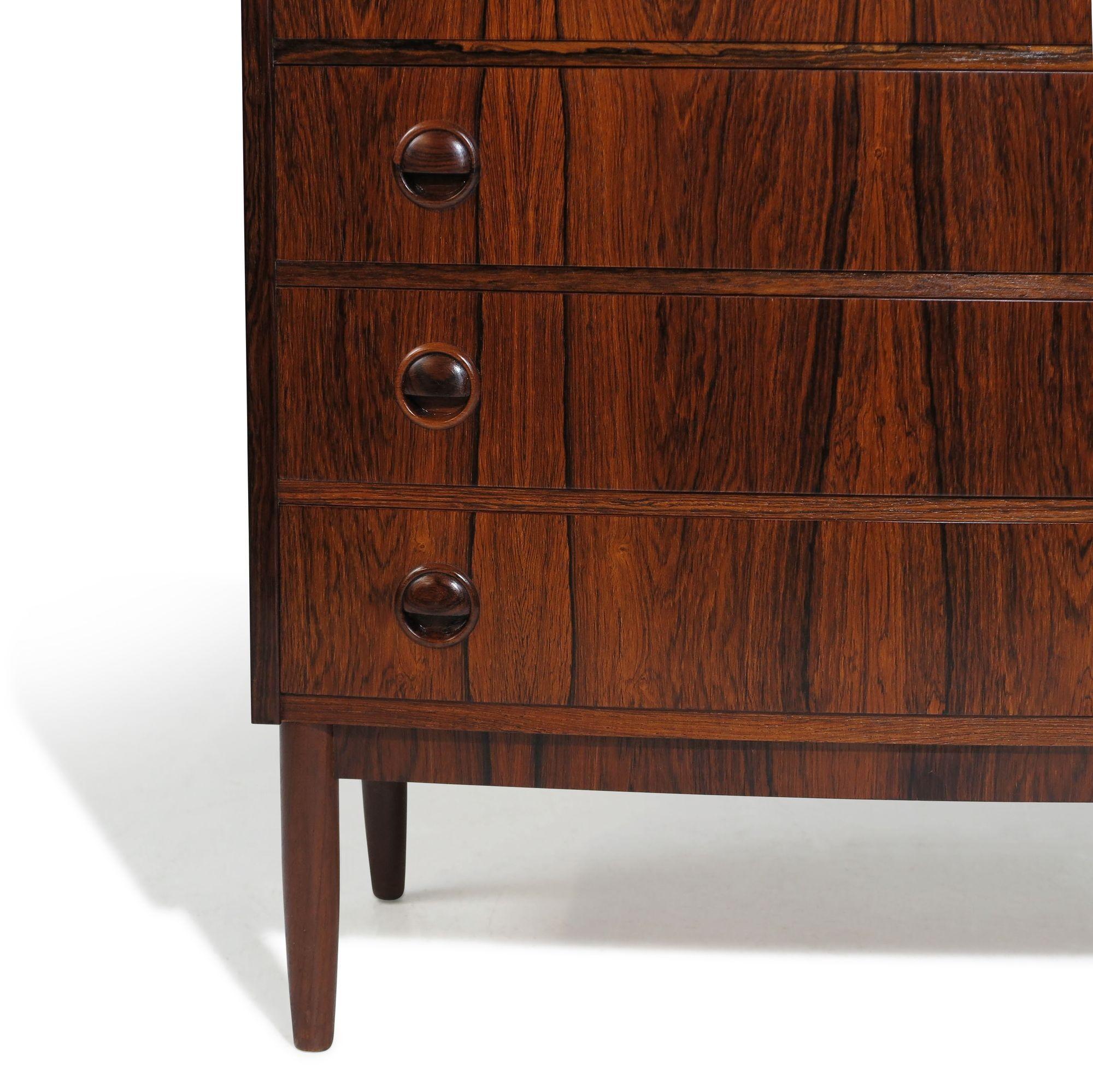 Danish tall dresser, finely handcrafted from Brazilian rosewood, features mitered corners and beautifully grained rosewood with pattern-matched drawer fronts, each adorned with circular carved pulls. The top drawer is equipped with a locking