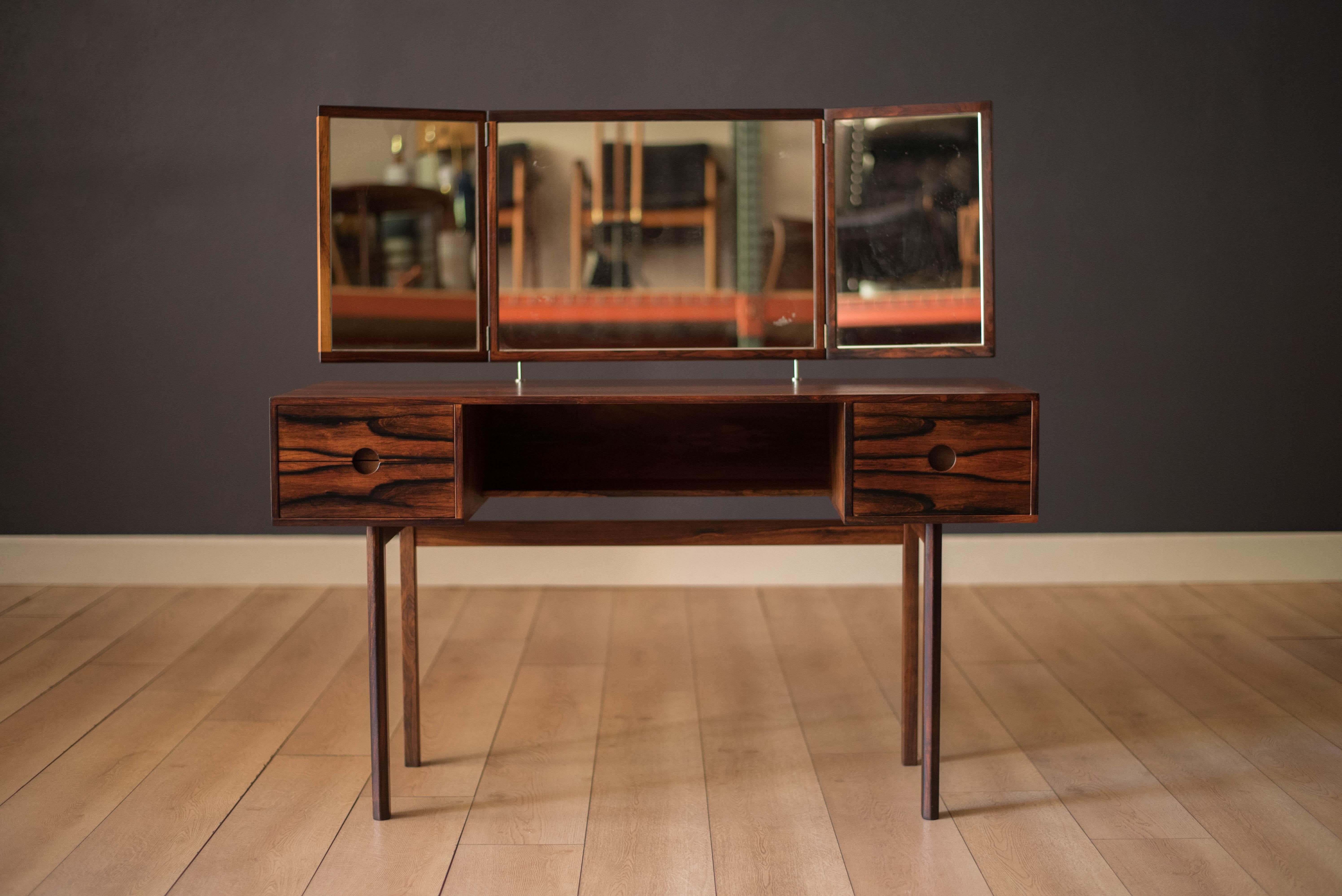 Mid-Century Modern vanity dressing table in rosewood designed by Kai Kristiansen for Aksel Kjersgaard, Denmark. Features sleek circular recessed pulls that open three dovetail storage drawers and includes one center fixed shelf. The floating mirror