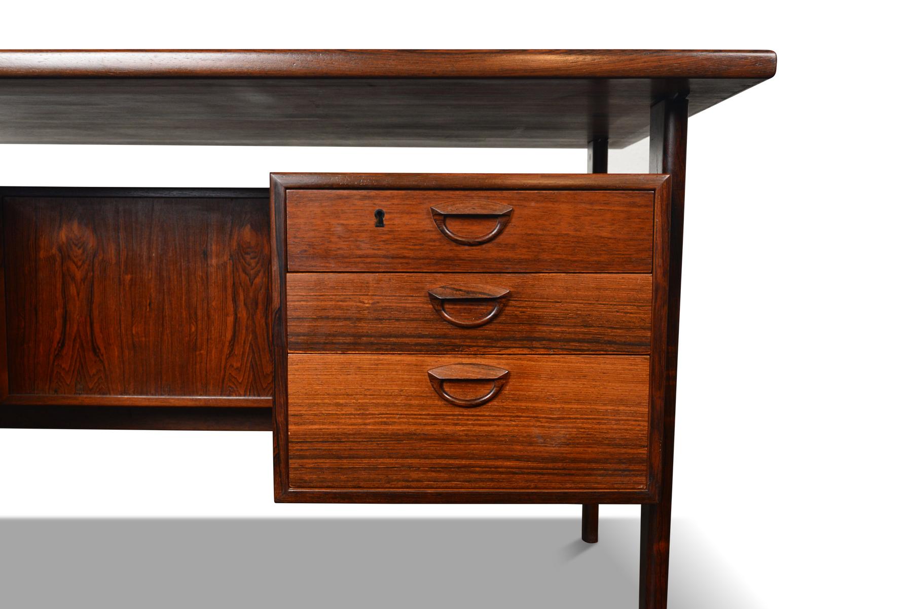 This Danish modern executive desk Model FM 60 in Brazilian rosewood was designed by Kai Kristiansen for Feldballes Møbelfabrik in 1957. The large work surface is supported by four sculpted legs which key into place. The kneehole is nestled between