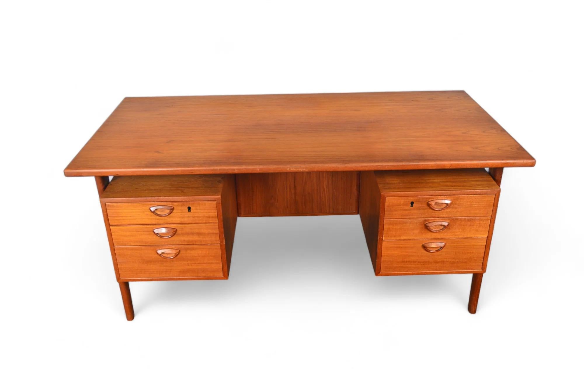 This Danish modern executive desk Model FM 60 in teak was designed by Kai Kristiansen for Feldballes Møbelfabrik in 1957. The large work surface is supported by four sculpted legs which key into place. The kneehole is nestled between two banks of