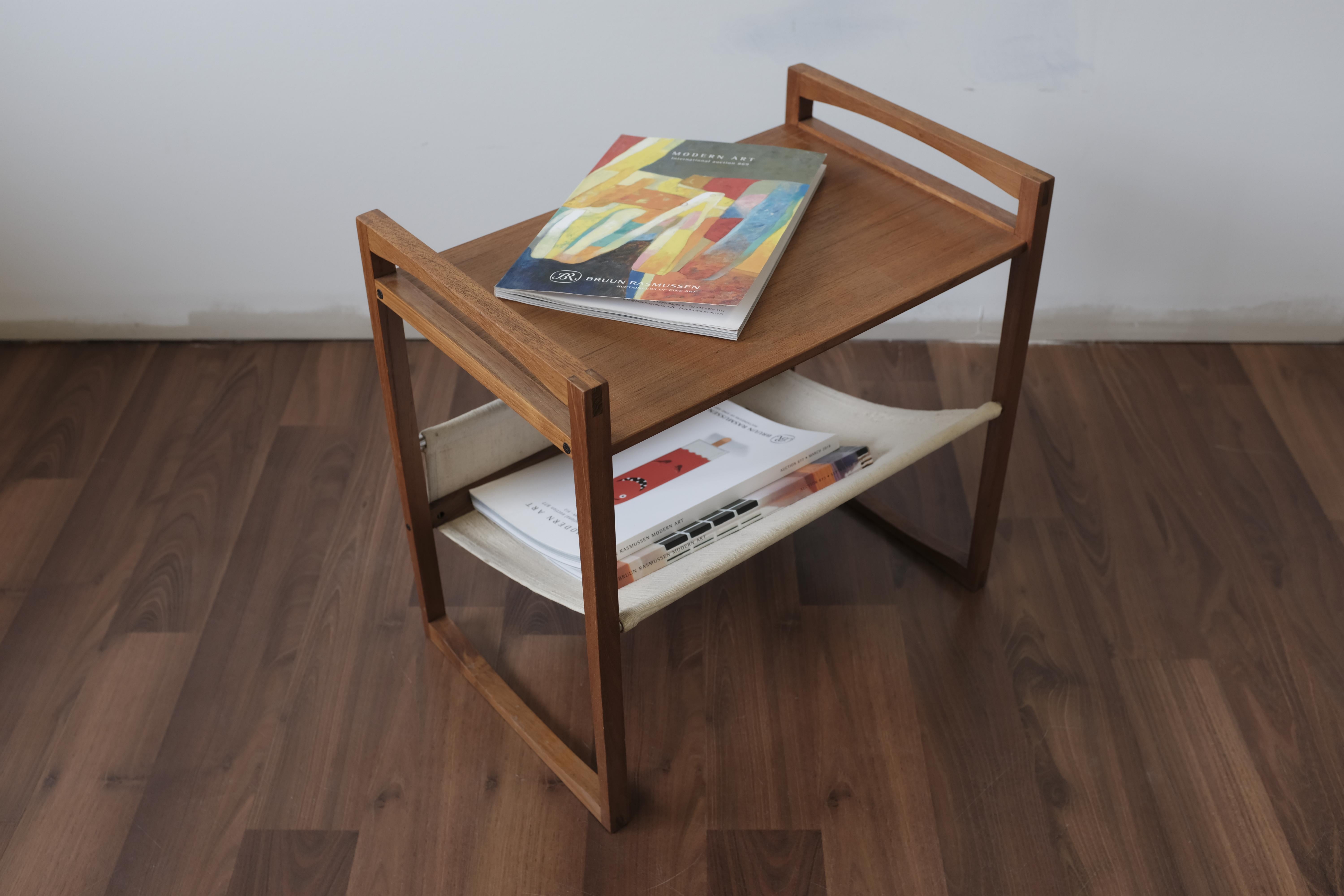 Small teak table with an angled linen rack for magazines, designed by Kai Kristiansen and manufactured by Sika Møbler. Bridal-jointed solid teak end frames are joined to the table top and stretcher using bolts. The linen rack can be positioned to