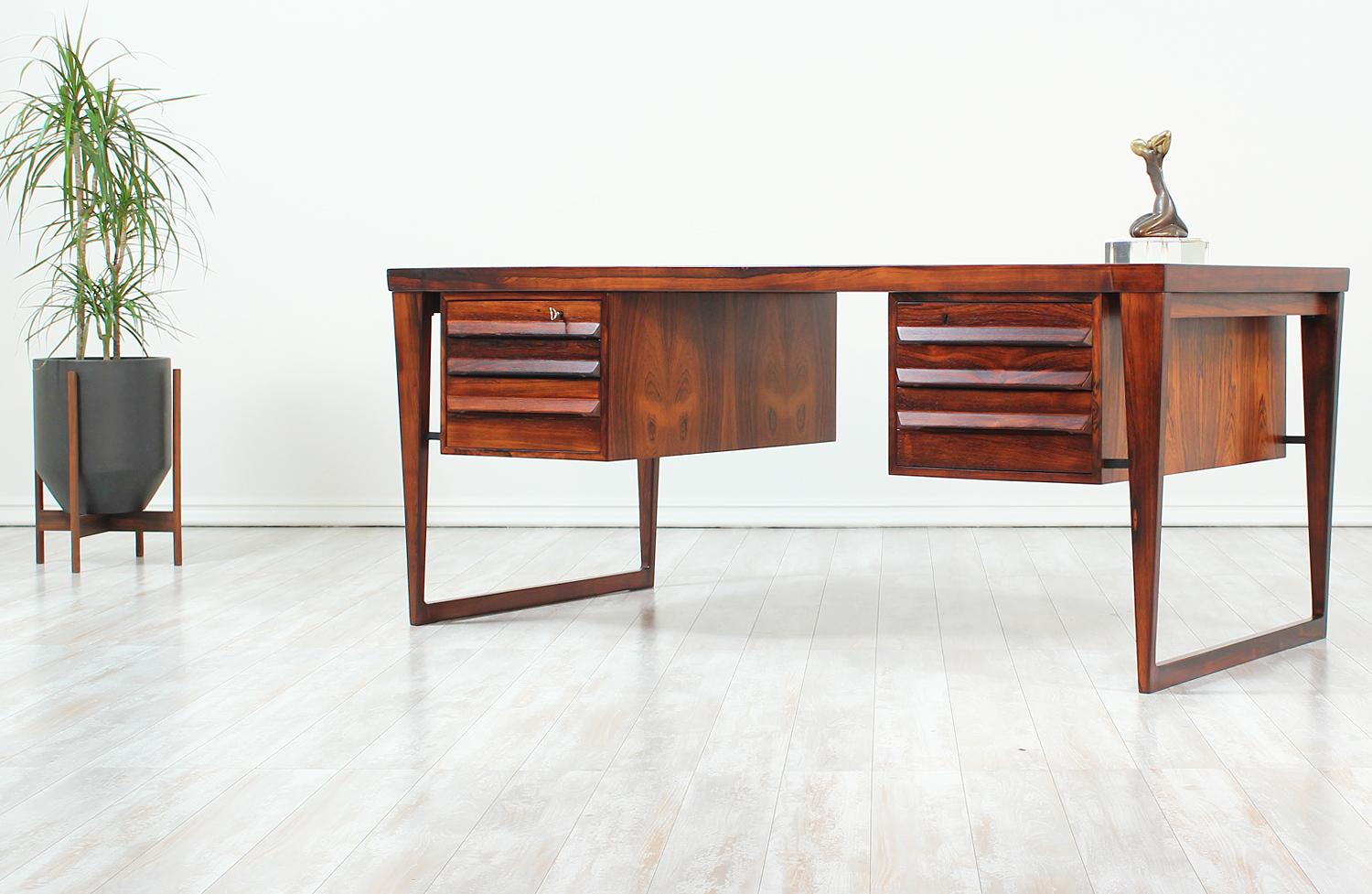 Iconic Model-70 desk designed by Kai Kristiansen for Feldballes Møbelfabrik in Denmark circa 1960s. This executive desk was meticulously crafted in rosewood and features a large surface top supported by a sled style base. Featuring plenty of storage