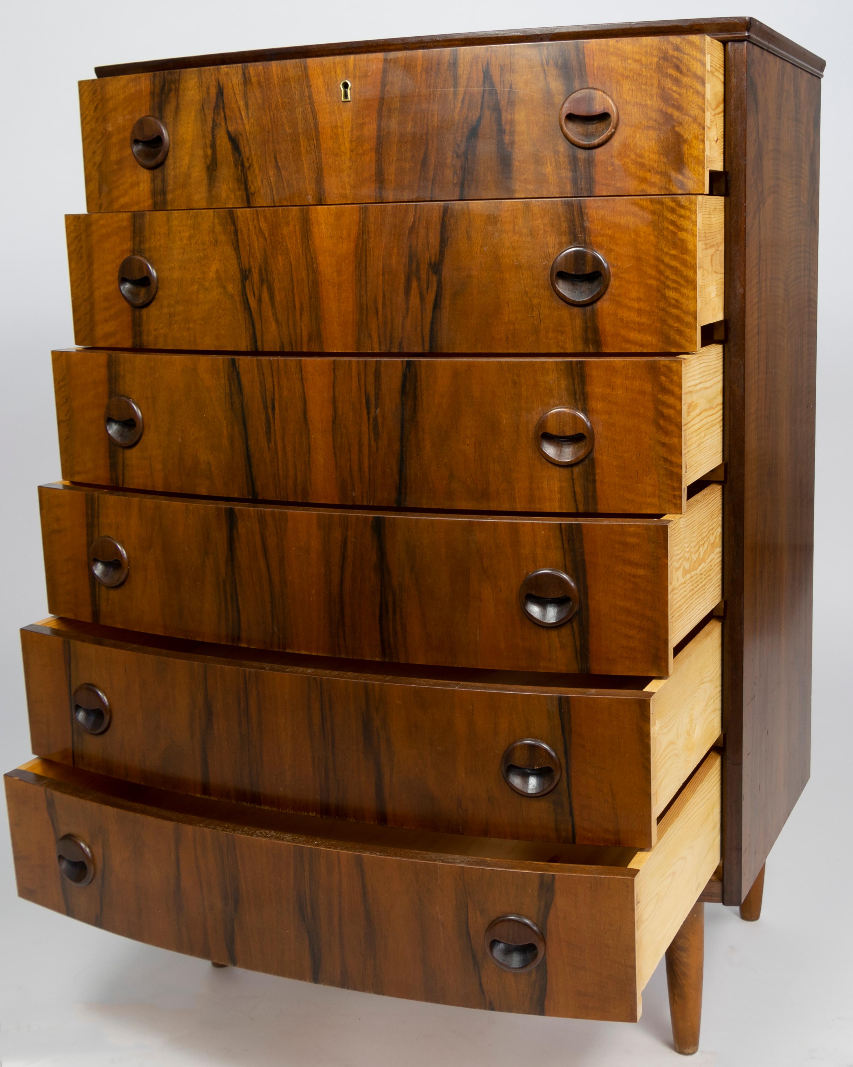 Beautiful Kai Kristensen chest of drawers in rosewood. 
The chest is Bow-fronted rosewood veneer with solid, sculpted rosewood drawer pulls. Afromosia teak legs.

Kristiansen finished his apprenticeship as a carpenter in 1947. Then he attended until