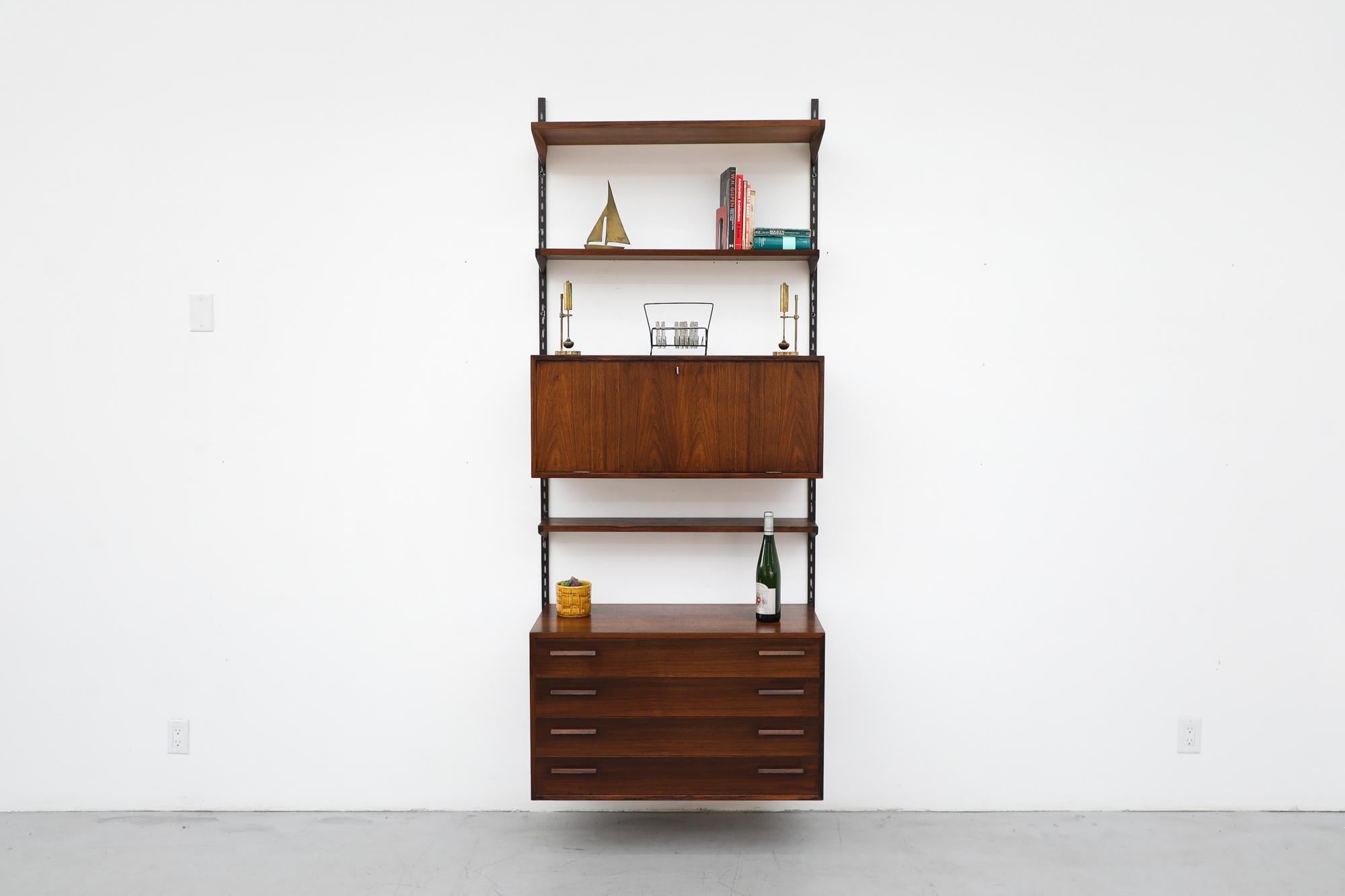 Charming midcentury wall-mount shelving system with locking drop down bar and lower dresser by Kai Kristiansen. Lightly refinished rosewood frame with carved drawer handles on metal brackets. In Impressive condition with light wear consistent with