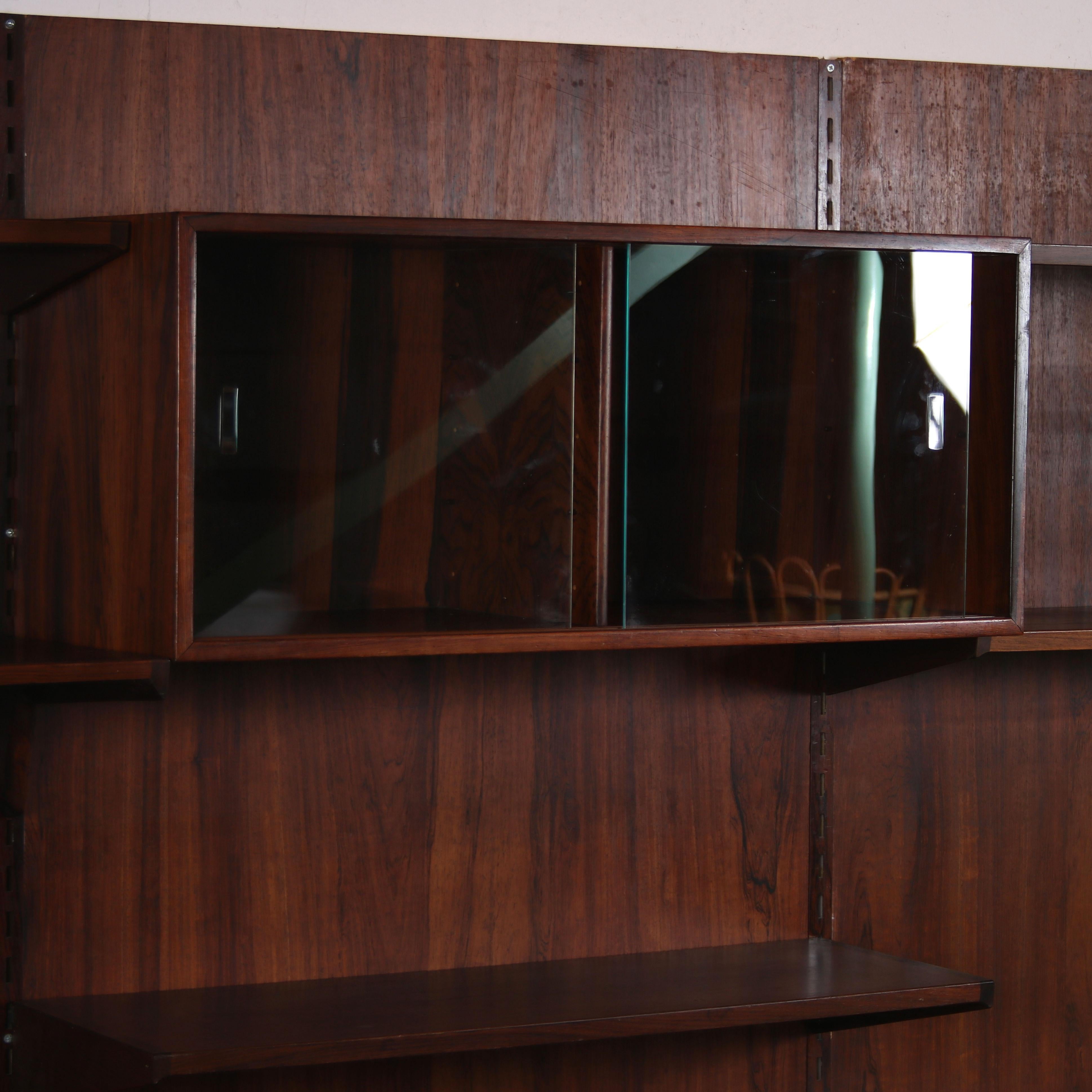 A beautiful, 3-unit wide wall mounted system cabinet desined by Kai Kristiansen and manufactured by FM Mobler in Denmark around 1950.

This large piece is made of high quality warm brown wood with metal details. The system structure of the piece