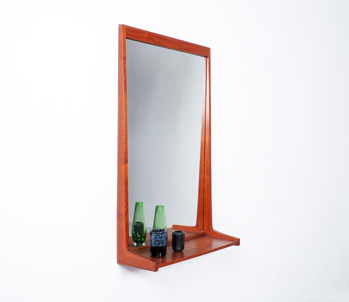 A teak wall mirror designed by Kai Kristiansen in the 1950's. Produced by Aksel kjersgaard, model 180. A mirror with a teak frame featuring a small shelf. 