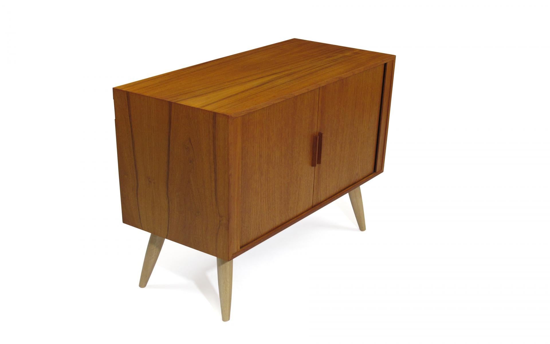 Midcentury Danish modern teak cabinet designed by Kai Kristiansen, manufactured in Denmark. Cabinet crafted of teak with tambour doors, and adjustable interior shelf, raised on solid oak tapered legs. Cabinet is fully restored in an excellent