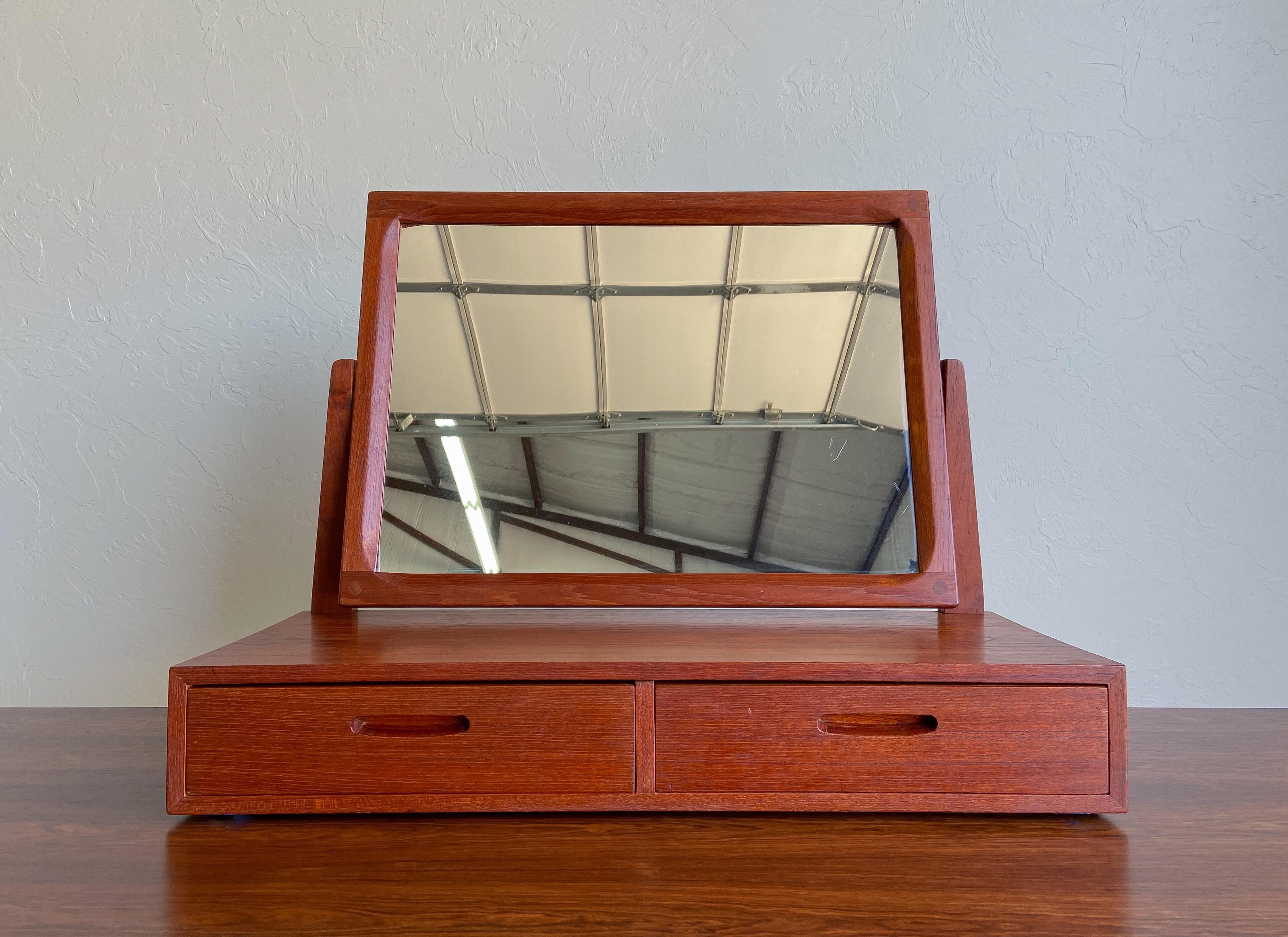 Angeboten wird ein ungewöhnlicher Tischspiegel, entworfen von Kai Kristiansen und hergestellt von Aksel Kjersgaard.

Die Konstruktion aus massivem Teakholz mit freiliegenden Tischlerarbeiten am Spiegelrahmen. Zwei Schubladen sind ideal für die