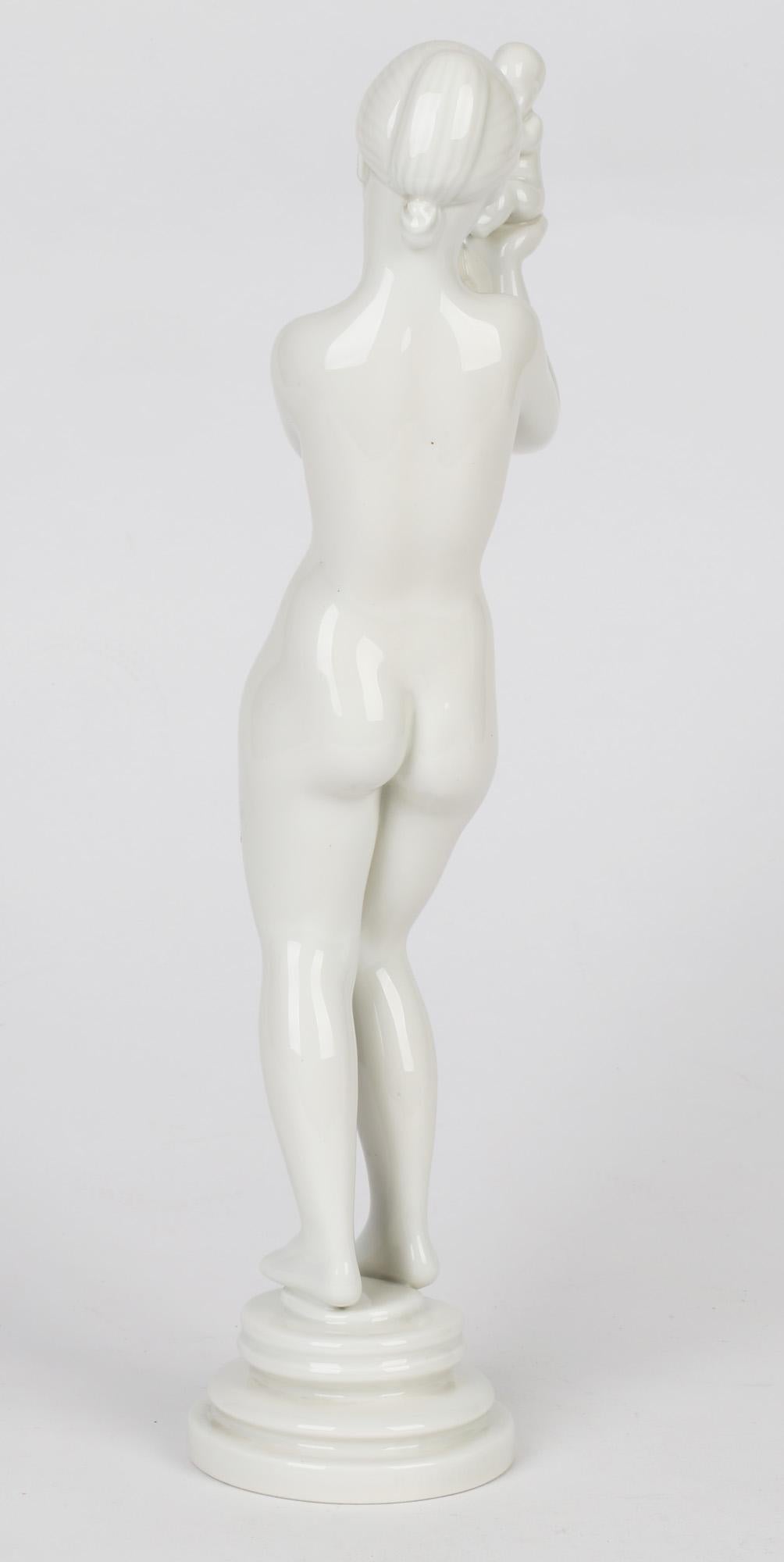 A stylish Danish porcelain Mother & Child sculptural figure designed by Kai Nielsen (1882-1924) for Bing & Grondhal and dating from the early 20th century. The figure portraying a naked girl stands on a rounded pedestal base with a young baby