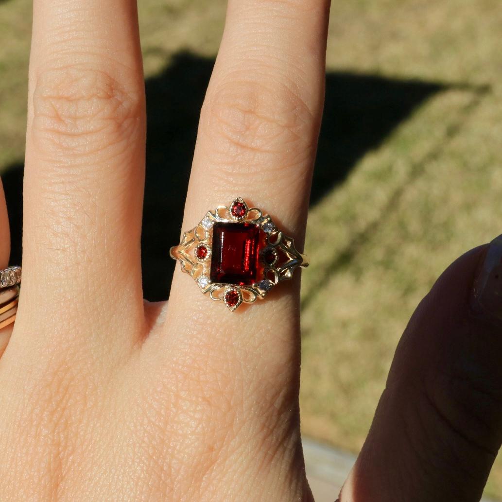 Rich, bold, and full of character, the Kai Renaissance Garnet Diamond Cocktail Ring is a true standout. At its center, a deep red emerald-cut garnet catches the light, framed by round garnet accents and diamonds. Set in 14K solid gold, the intricate
