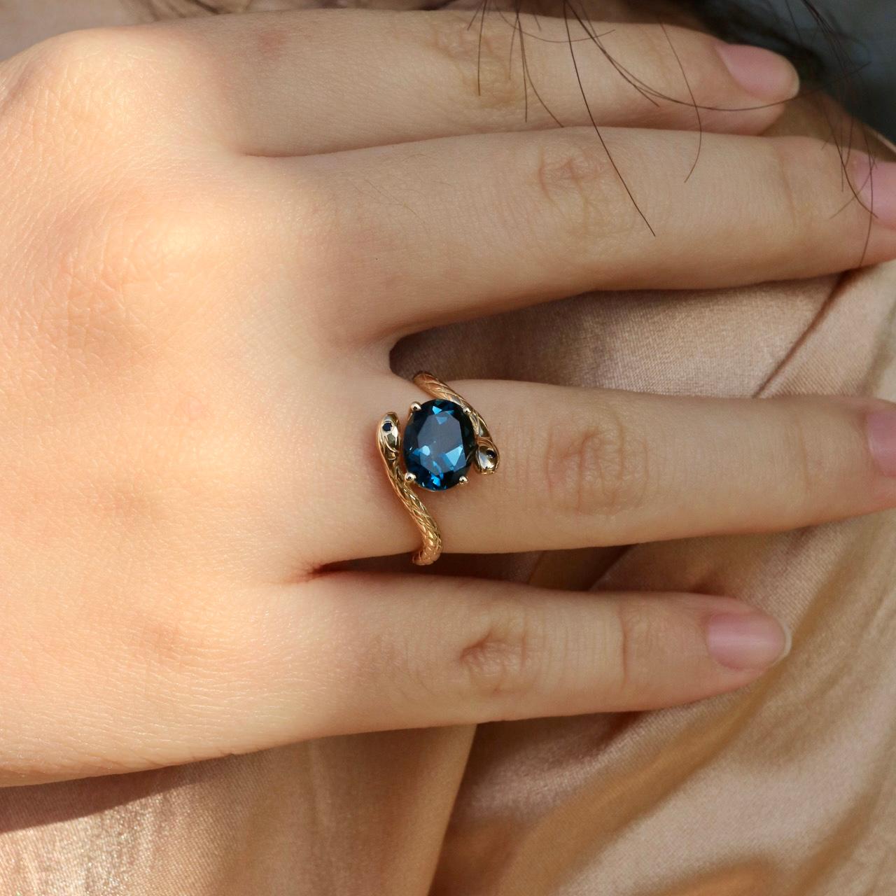 Audacieuse, élégante et intemporelle, cette bague Kai Snake London Blue Topaz Sapphire East-West met en valeur une topaze bleue naturelle de Londres sertie dans le sens est-ouest. La pierre précieuse est rehaussée de deux saphirs naturels bleu