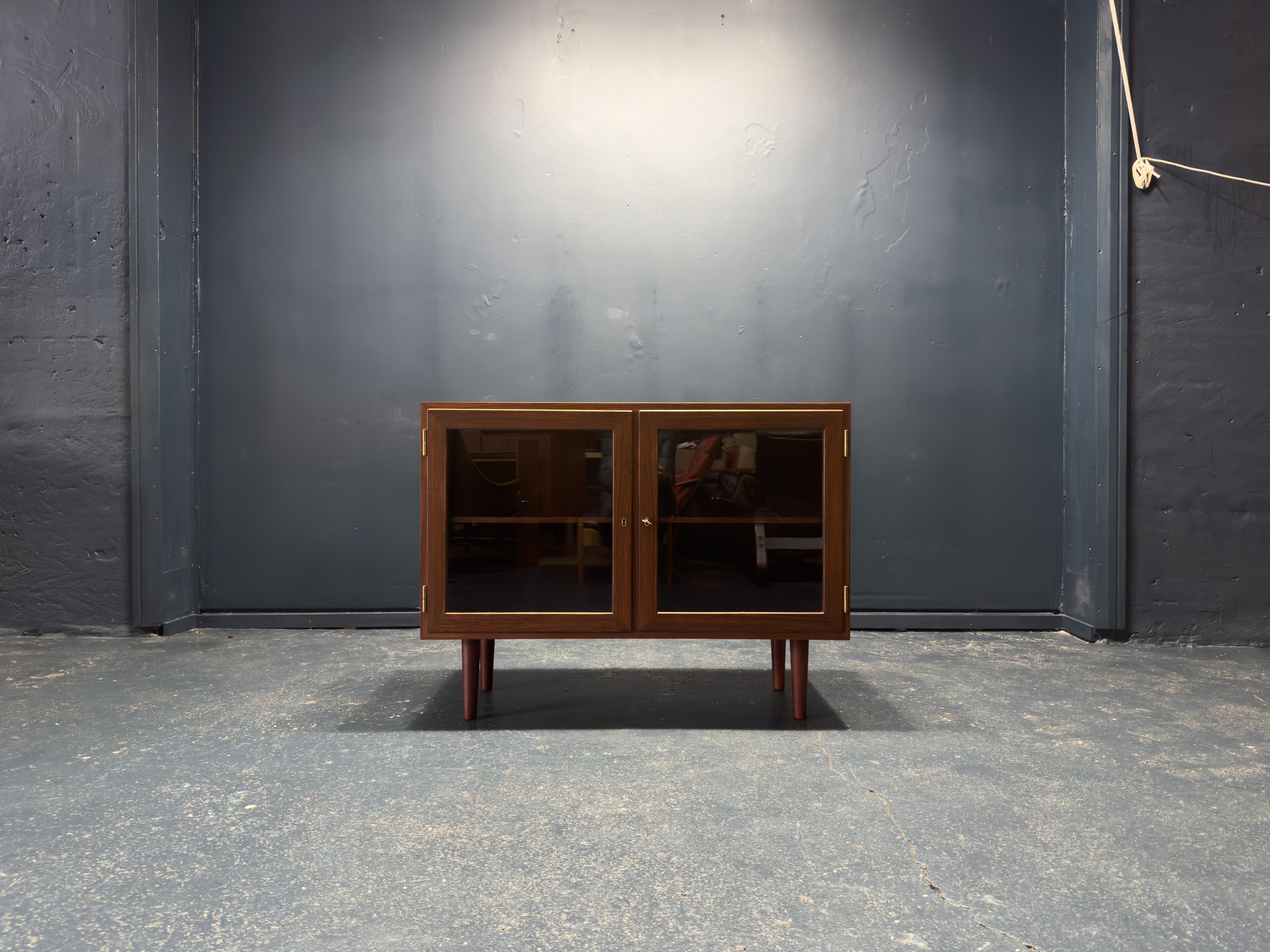 This hardwood and glass sideboard, designed in the 1960s by Kai Winding for P. Jeppesen Furniture, is a refined example of Danish craftsmanship. Constructed from rich hardwood, the cabinet showcases an exquisite grain pattern that adds warmth and