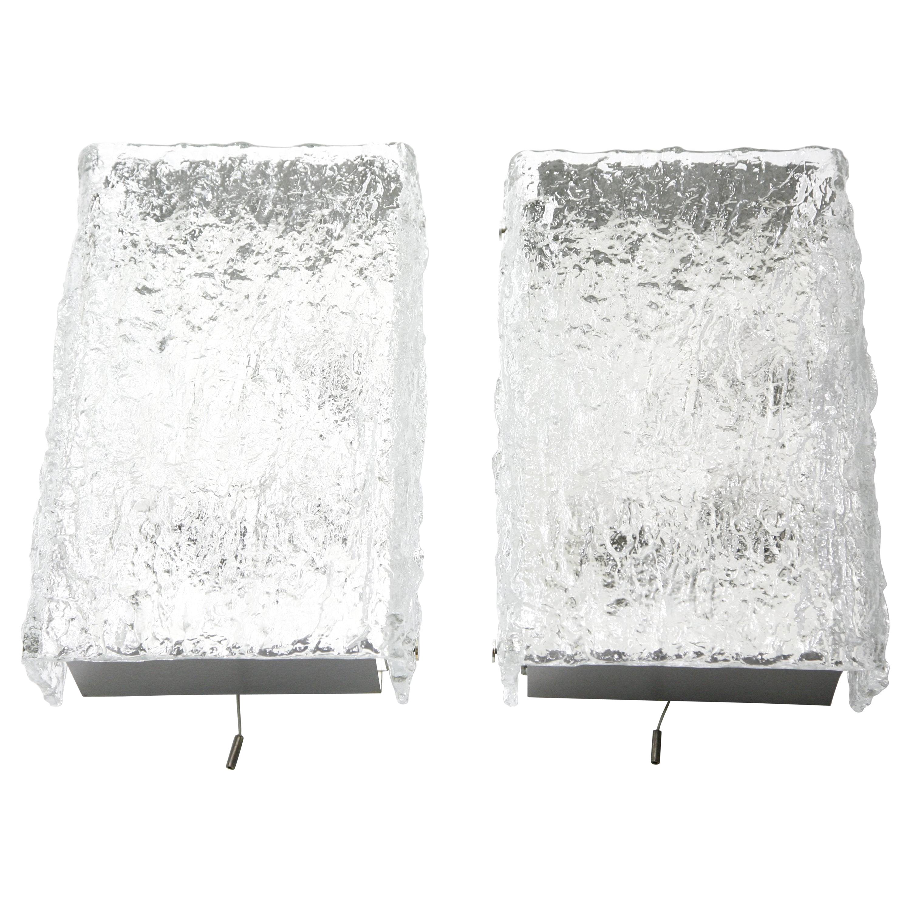 Pair of wall lights by Kalmar from the 1960s white enameled back plates, top and bottom plates are matte nickel, one piece of thick ice looking bend crystal with a wavy structure to the outer glass surface glass shade with four chrome fittings holds
