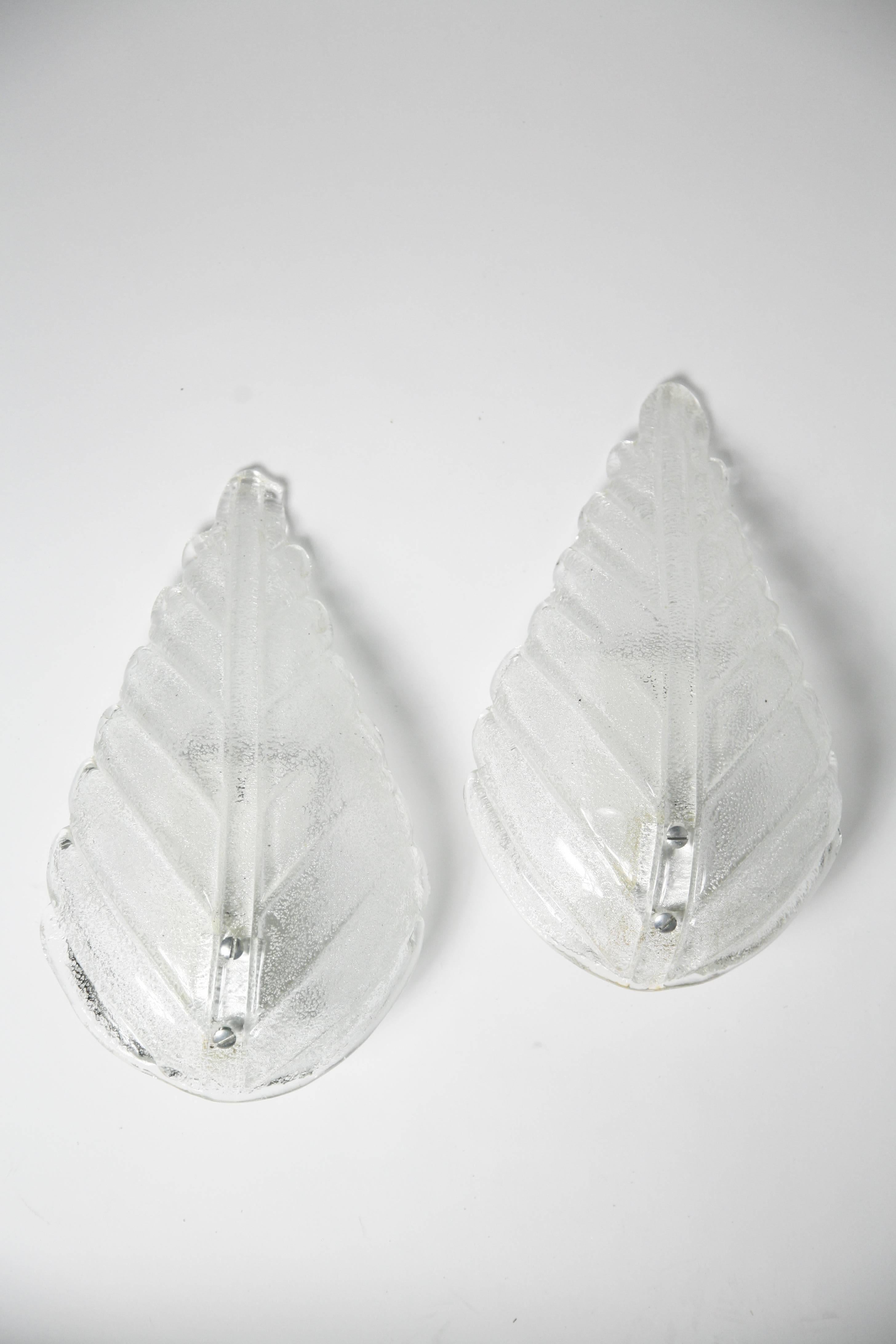 Pair of sconces by Kaiser Leuchten from 1970s white enameled back plates and a shade of glass shaped as a leaf, on the inside are tiny glass pieces the size of cane sugar which makes them sparkle, holds one candelabra socket each.
Comes with silver