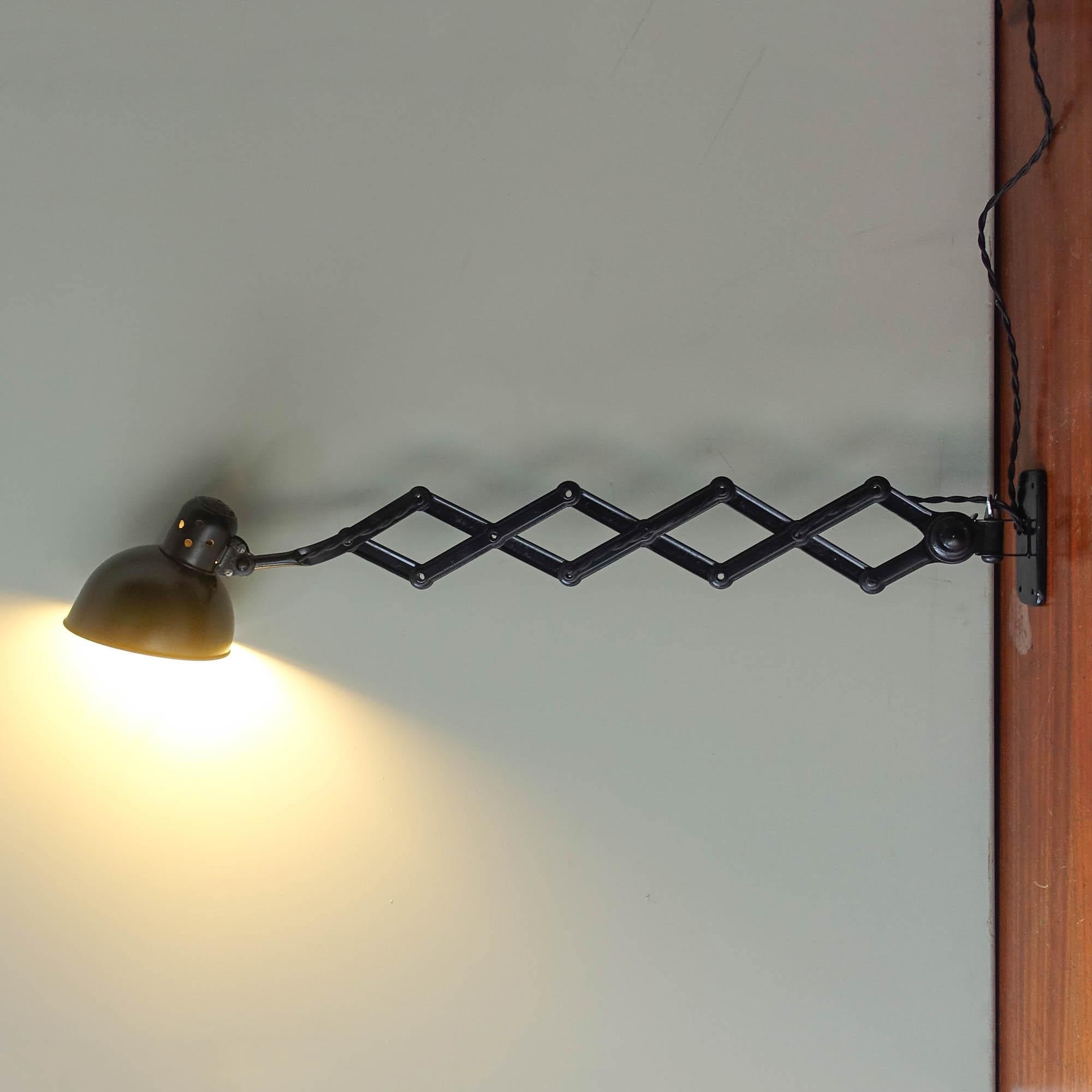 This 6718 model scissor arm wall lamp was designed in the 1930's by Christian Dell, and manufactured by Kaiser Idell. It features an adjustable black lacquered metal shade, with an adjustable scissor arm, that extends up to 90 cm long. Very