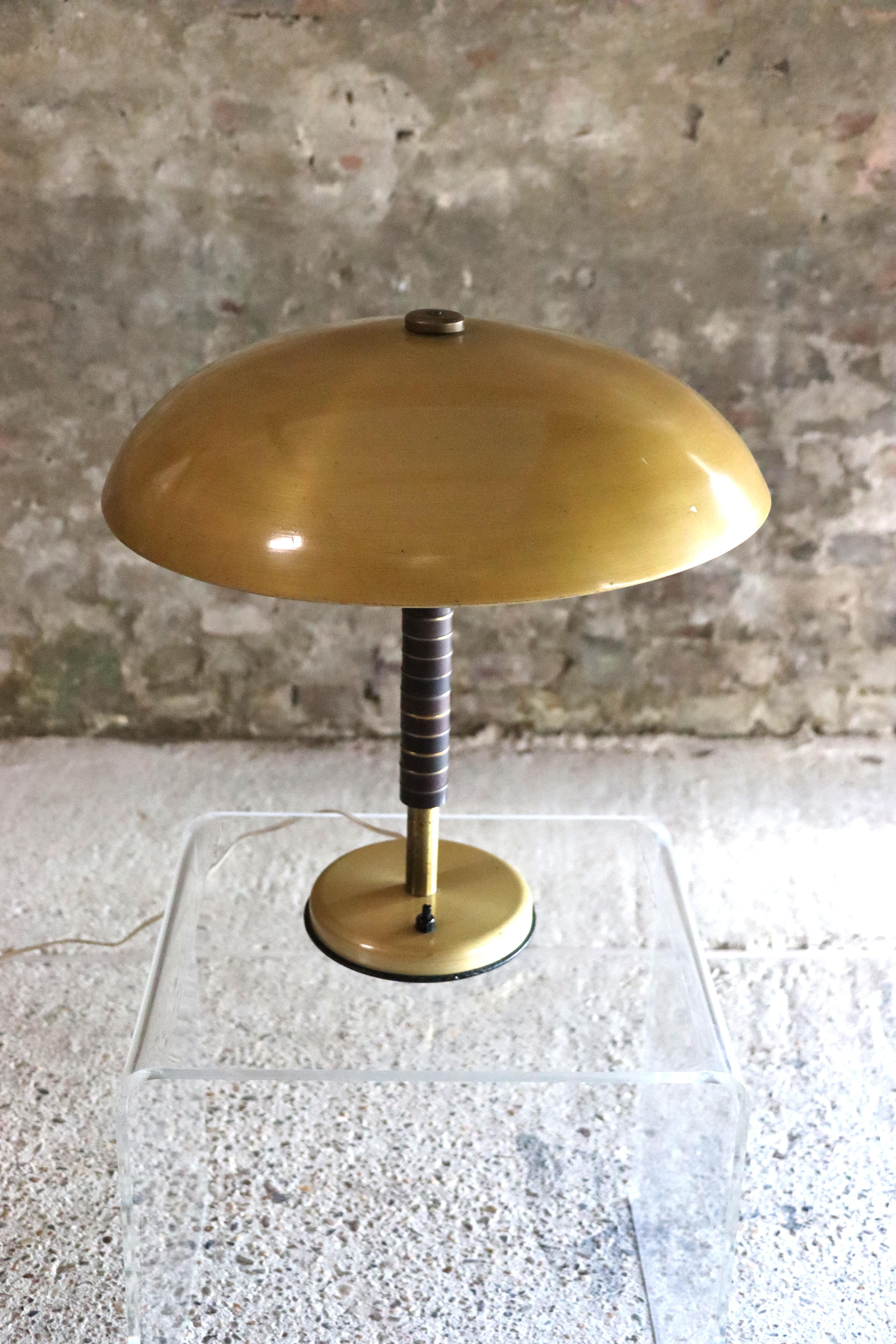 This cool table lamp dates back to 1944 and has a brass base and bakelite stem. The lampshade is aluminum teinted in brass color. The diffusion of the light is magnified by the aluminium that amplifies and reflects it smoothly. A real quality of