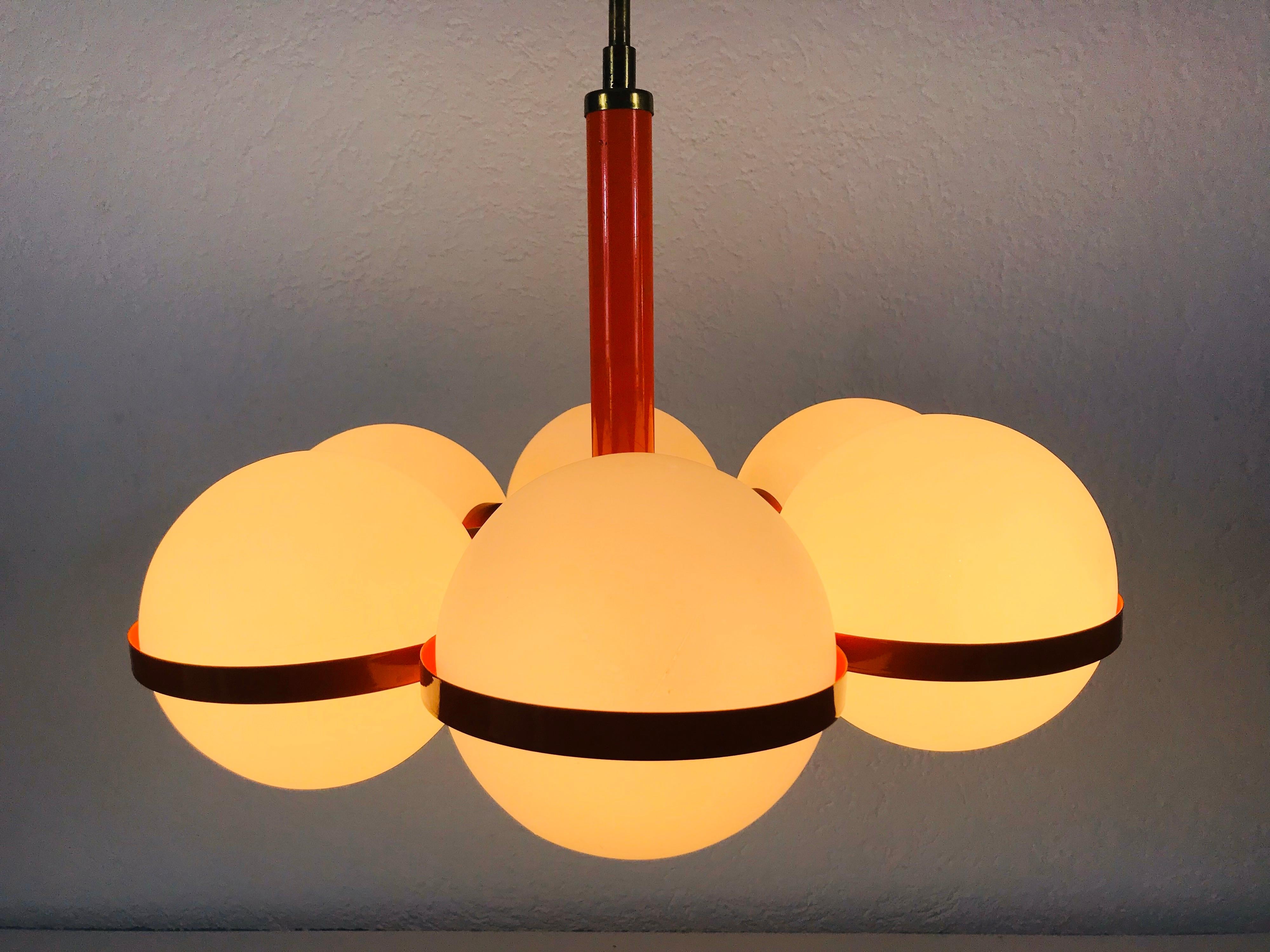 A midcentury chandelier by Kaiser made in Germany in the 1960s. It is fascinating with its space age design and six opaque balls. The red circular body of the light is made of full metal, including the arms.


The light requires six E14 light