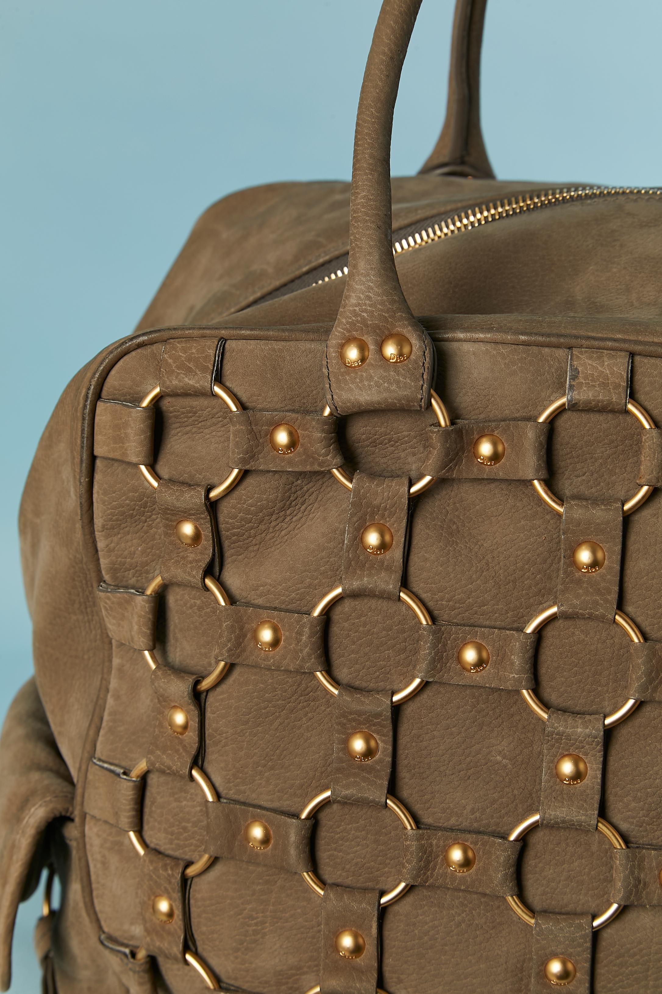 Sac en daim kaki à grande poignée supérieure avec des anneaux en métal doré et des clous de marque. Doublure en tissu brun foncé, probablement en rayonne. Fermeture à glissière centrale sur le dessus avec tirette de fermeture éclair de marque.