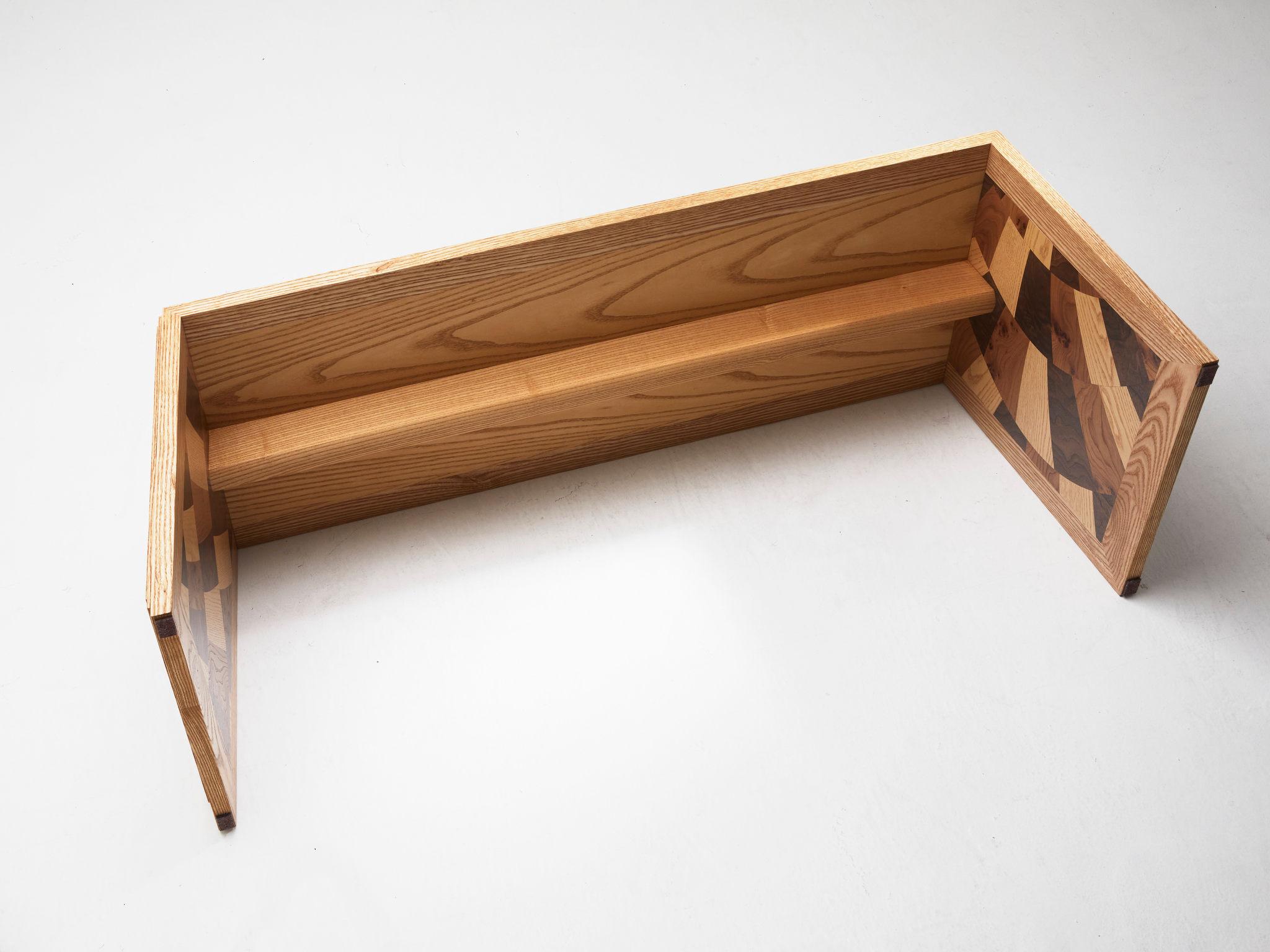 This Kaleidoscope bench is one of a pair executed in different veneers whilst retaining the same base material of American Ash.  
The listing you're looking at is made of Ash, Walnut and Elm, all woods at the warm, brown end of the spectrum.  
The