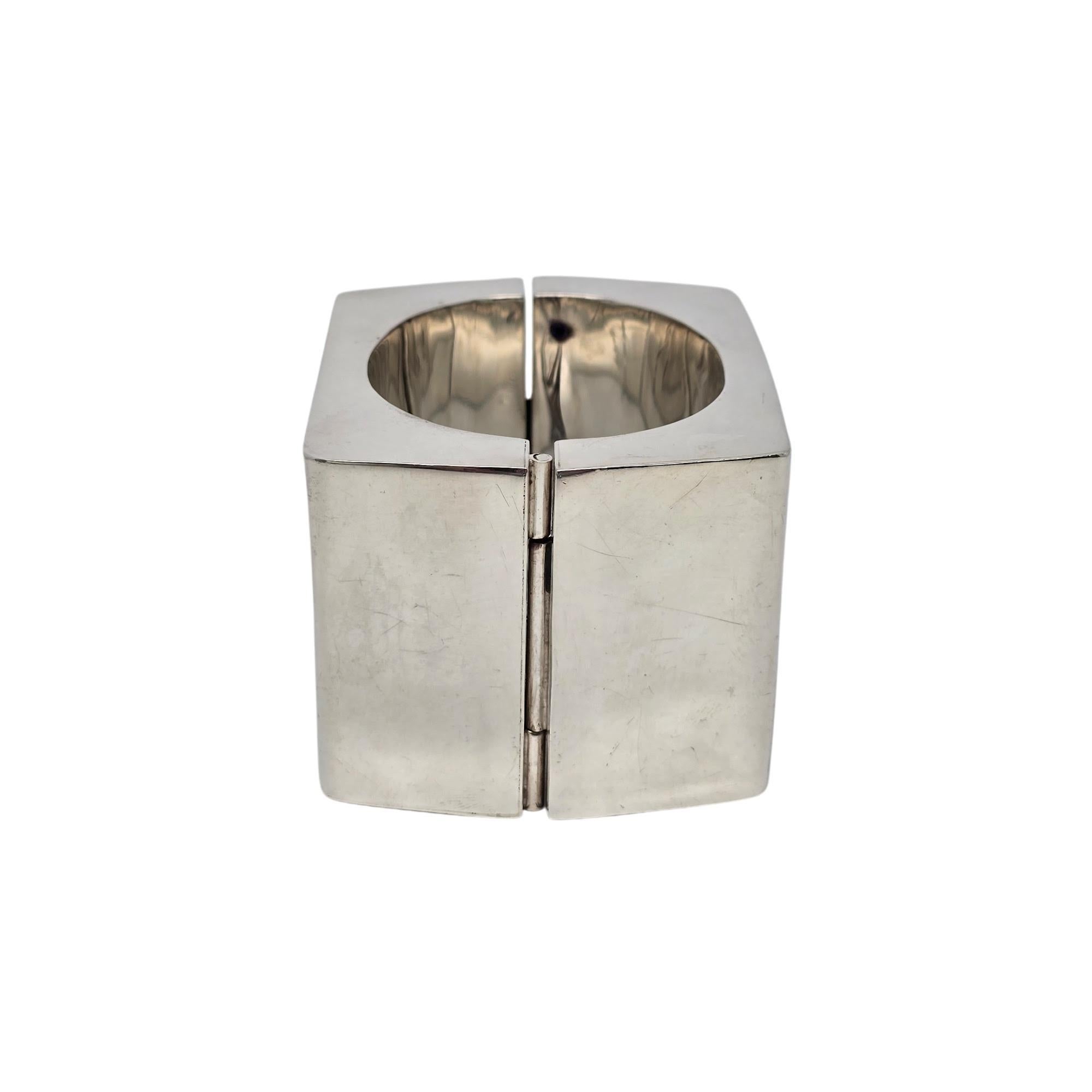 Kalibre by Harlene Korey großer quadratischer Armreif aus Sterlingsilber mit Scharnier.

CIRCA 1985, dieses große und kräftige Armband mit Scharnier zeigt ein geometrisches Design im modernistischen Stil.

Wiegt ca. 142,1g, 91,4dwt.

Der Innenumfang
