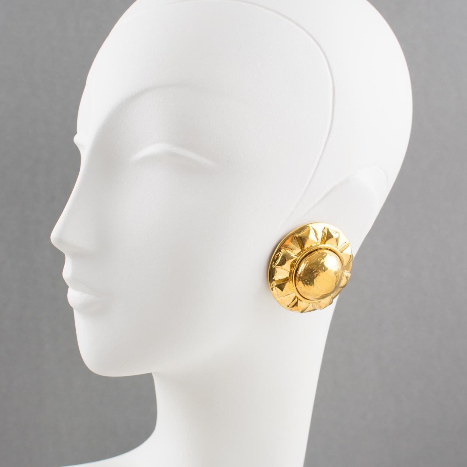 Estos elegantes pendientes de clip Kalinger Paris presentan una forma sobredimensionada y muy abombada, de resina recubierta de metal dorado, con un motivo de diseño tallado en forma de sol. No hay ninguna marca visible del diseñador.
Medidas: 4,3