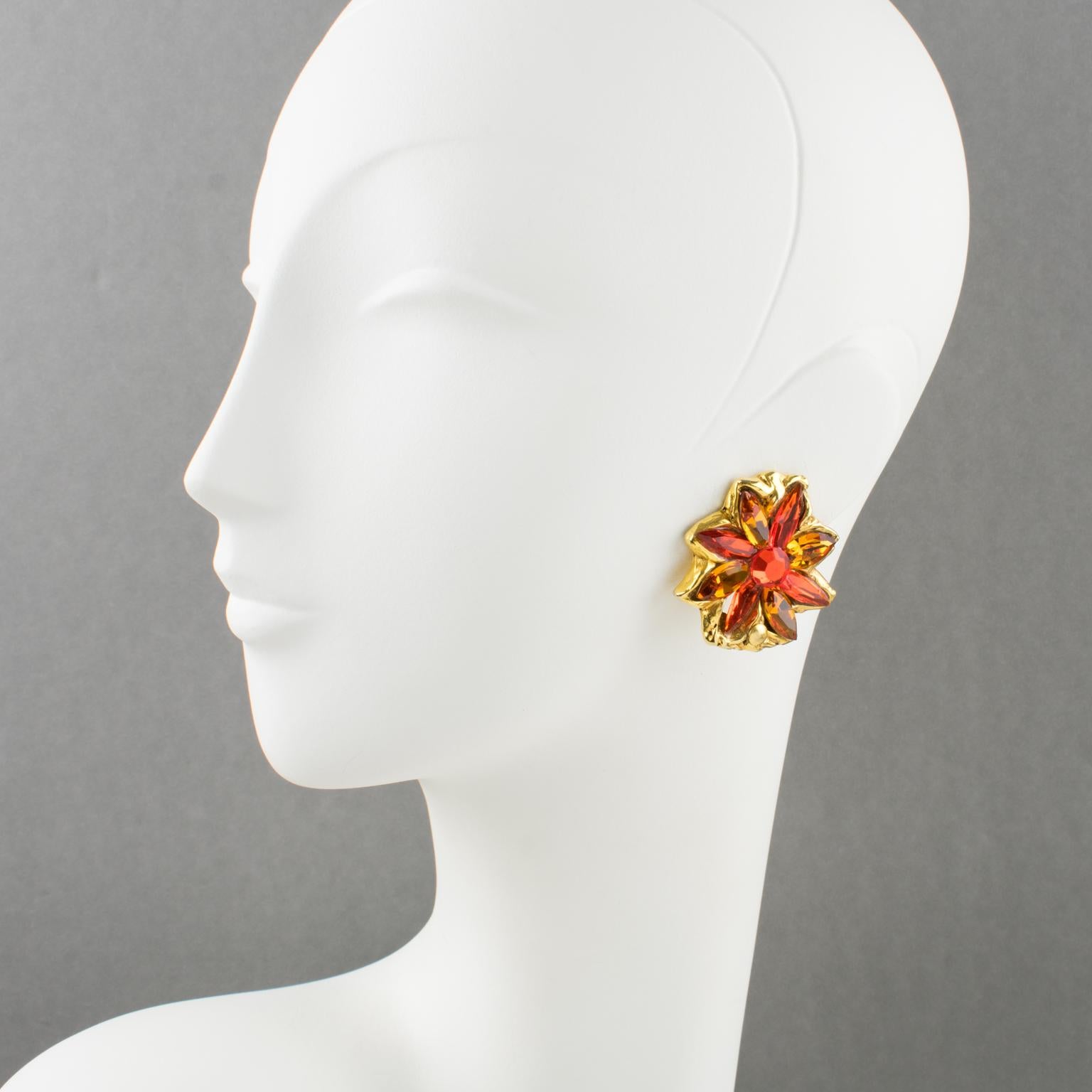 Diese eleganten Kalinger Paris Blumenohrringe haben eine übergroße Blumenform mit einer glänzenden, vergoldeten Metallumrandung, die mit feuerorangen und honigfarbenen, facettierten Strasssteinen besetzt ist. Sie sind auf der Rückseite mit dem