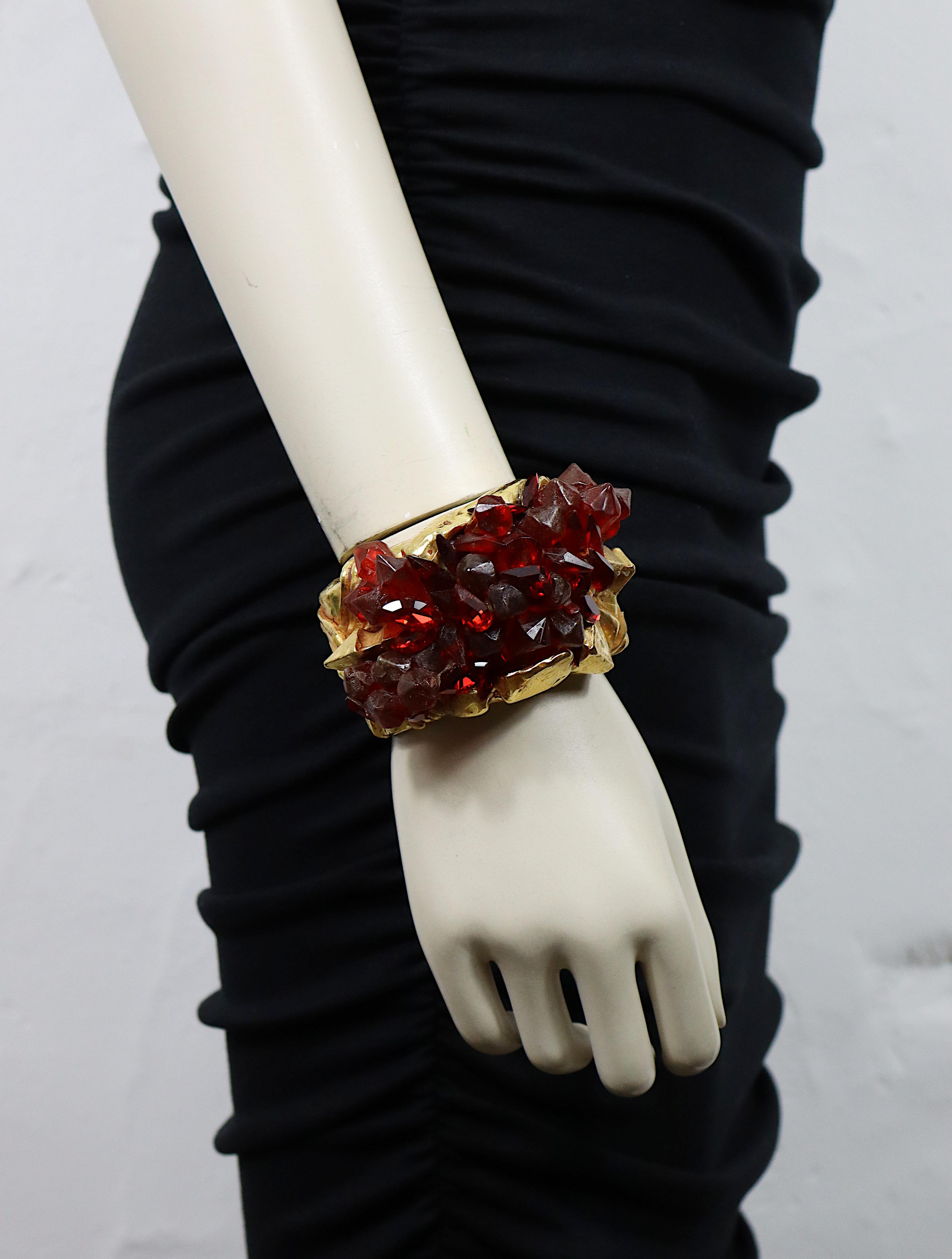 Pulsera puño KALINGER vintage de resina en tono dorado con un diseño de textura de roca adornado con cuentas de resina roja y cristales rojos que imitan un racimo de cuarzo.

KALINGER en relieve.

Medidas orientativas : medidas interiores aprox.