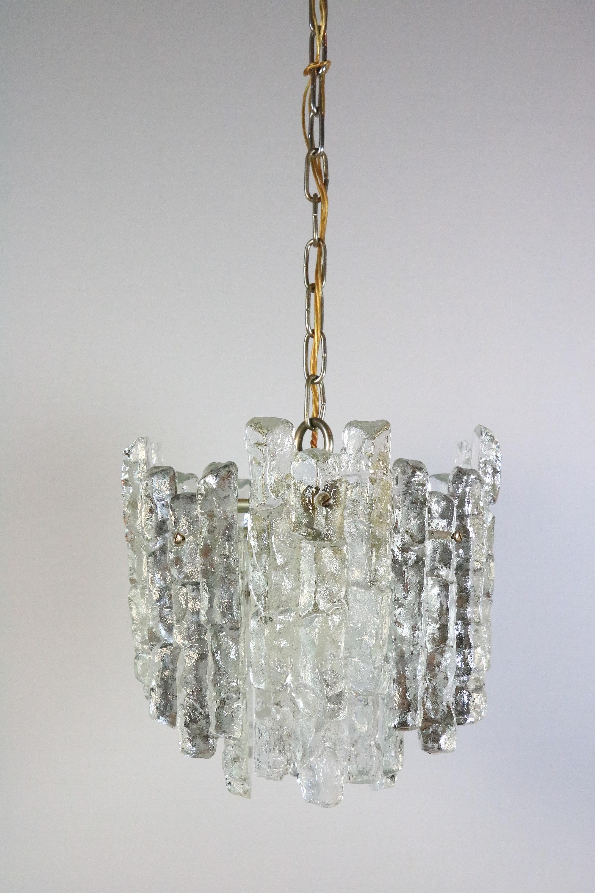 Very beautiful and decorative ice glass chandelier. Probably crystal glass.
By Kalmar, Austria

Manufactured in midcentury, circa 1970 (late 1960s or early 1970s). 

The lamp is made of 12 ice glass blocks in two rows which are mounted on a silver