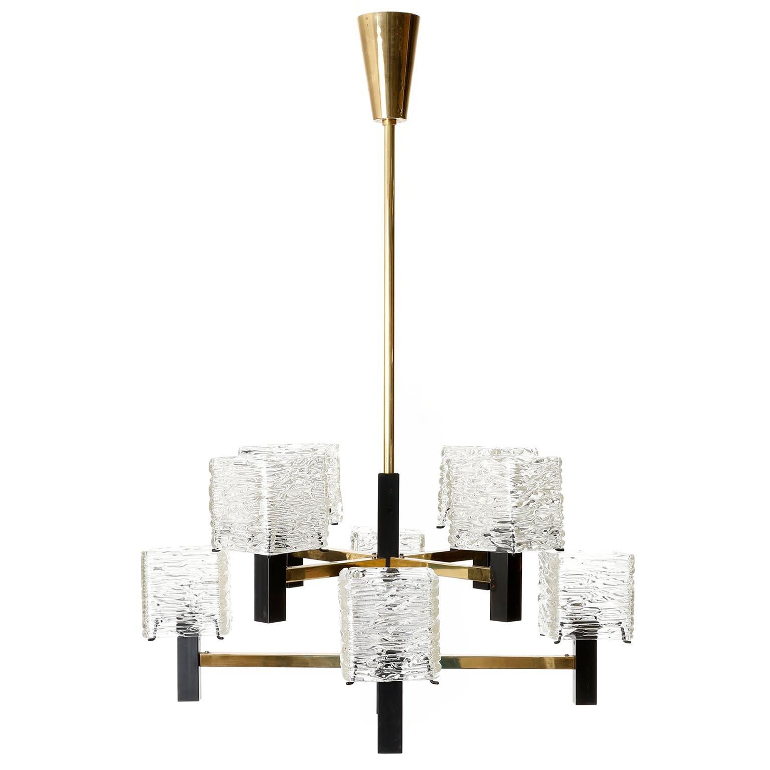 An eight-arm chandelier by J.T. Kalmar, Vienna, Austria, manufactured in midcentury, circa 1960 (late 1950s or early 1960s).
The fixture is made of a nice mixture of materials: square textured clear glass lamp shades, solid polished brass and black