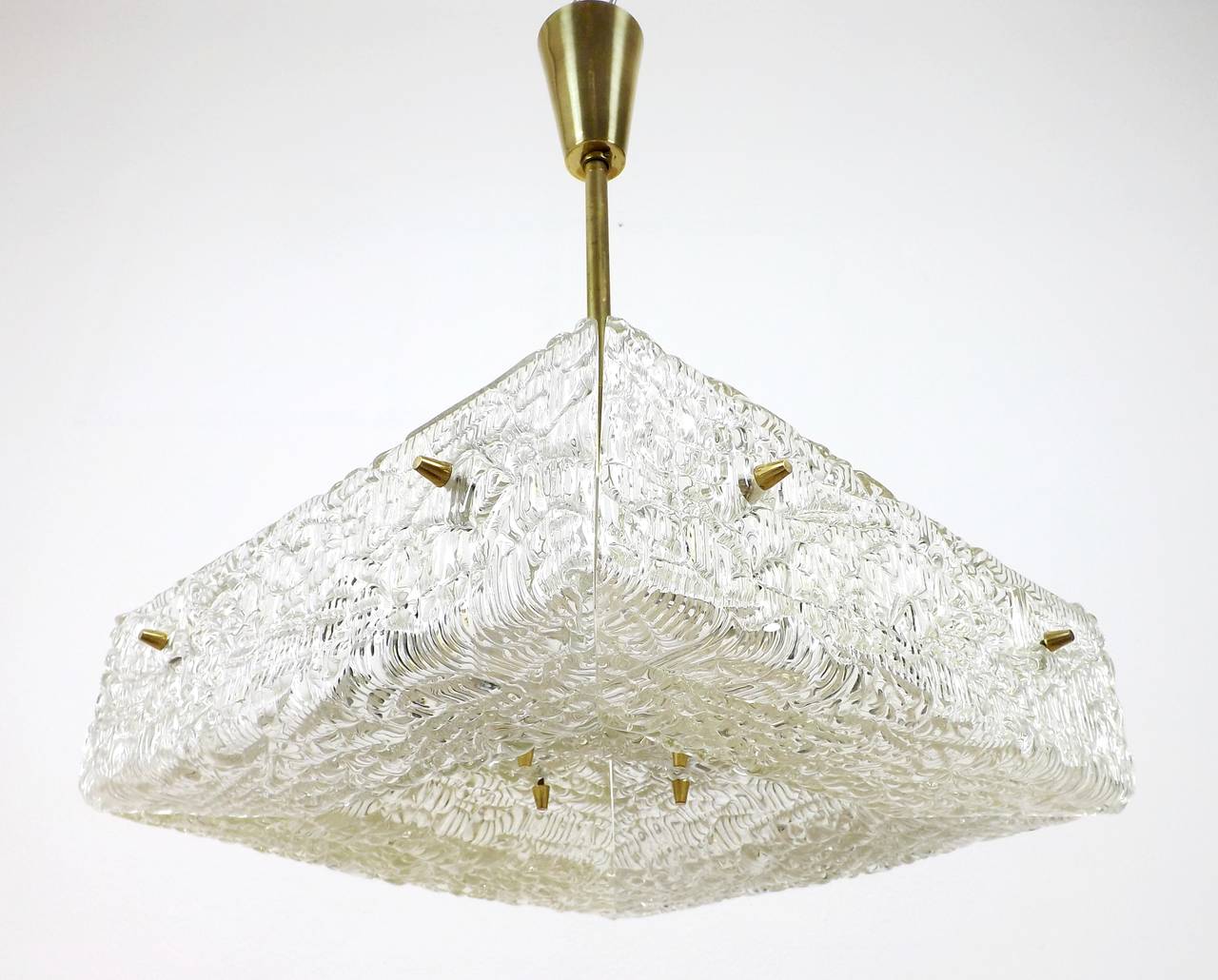 A textured glass and brass light fixture by J.T. Kalmar, Austria, manufactured in midcentury, circa 1960 (late 1950s or early 1960s).
A square pressed glass with a watery structure is divided into four parts which are mounted with cone shaped brass