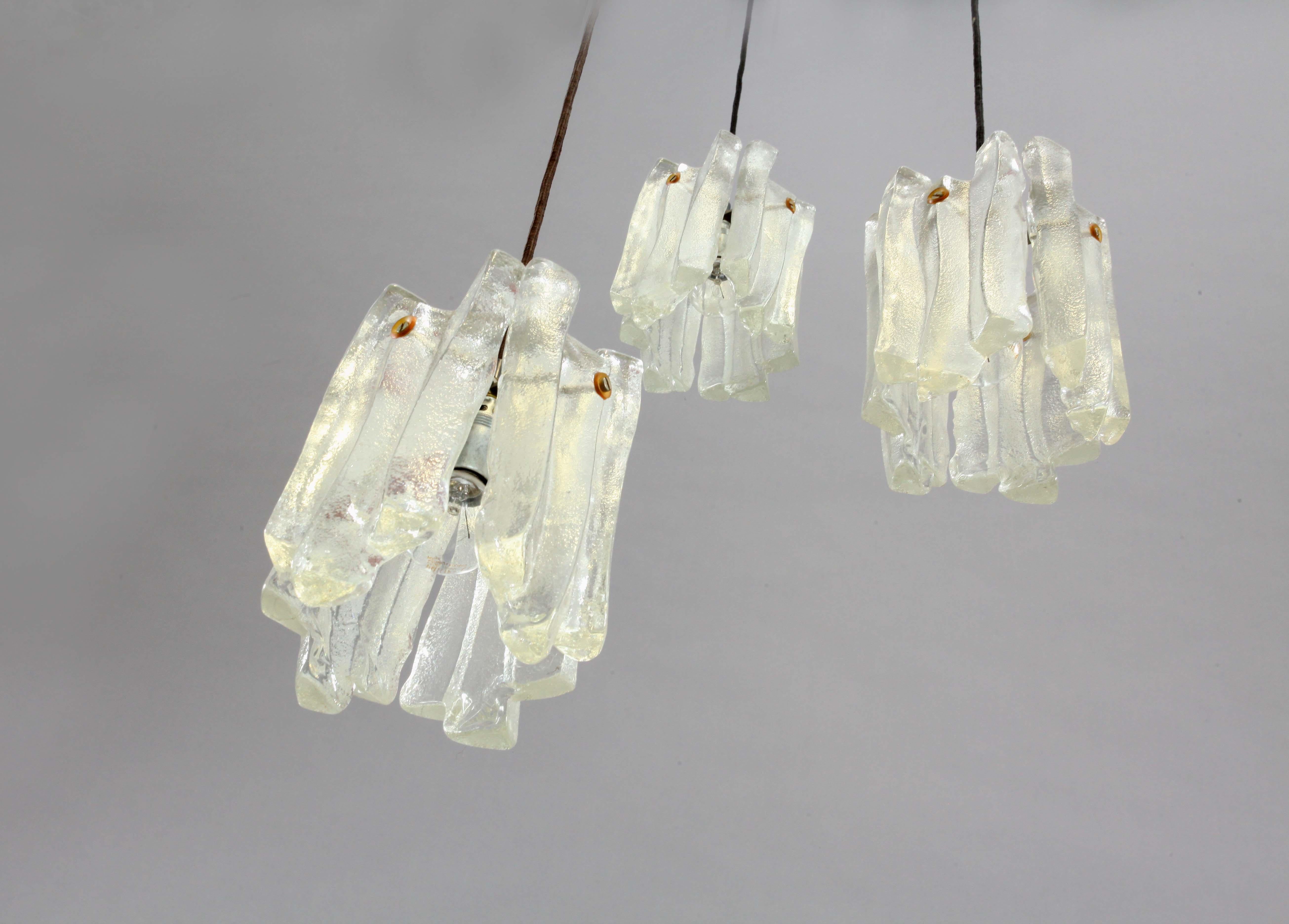 A hanging lamp by Kalmar, Austria, manufactured in midcentury, circa 1970 (end of 1960s and beginning of 1970s). It is made of three frosted ice glass lamp shades which are hanging on a white painted ceiling triangle plate with height adjustable