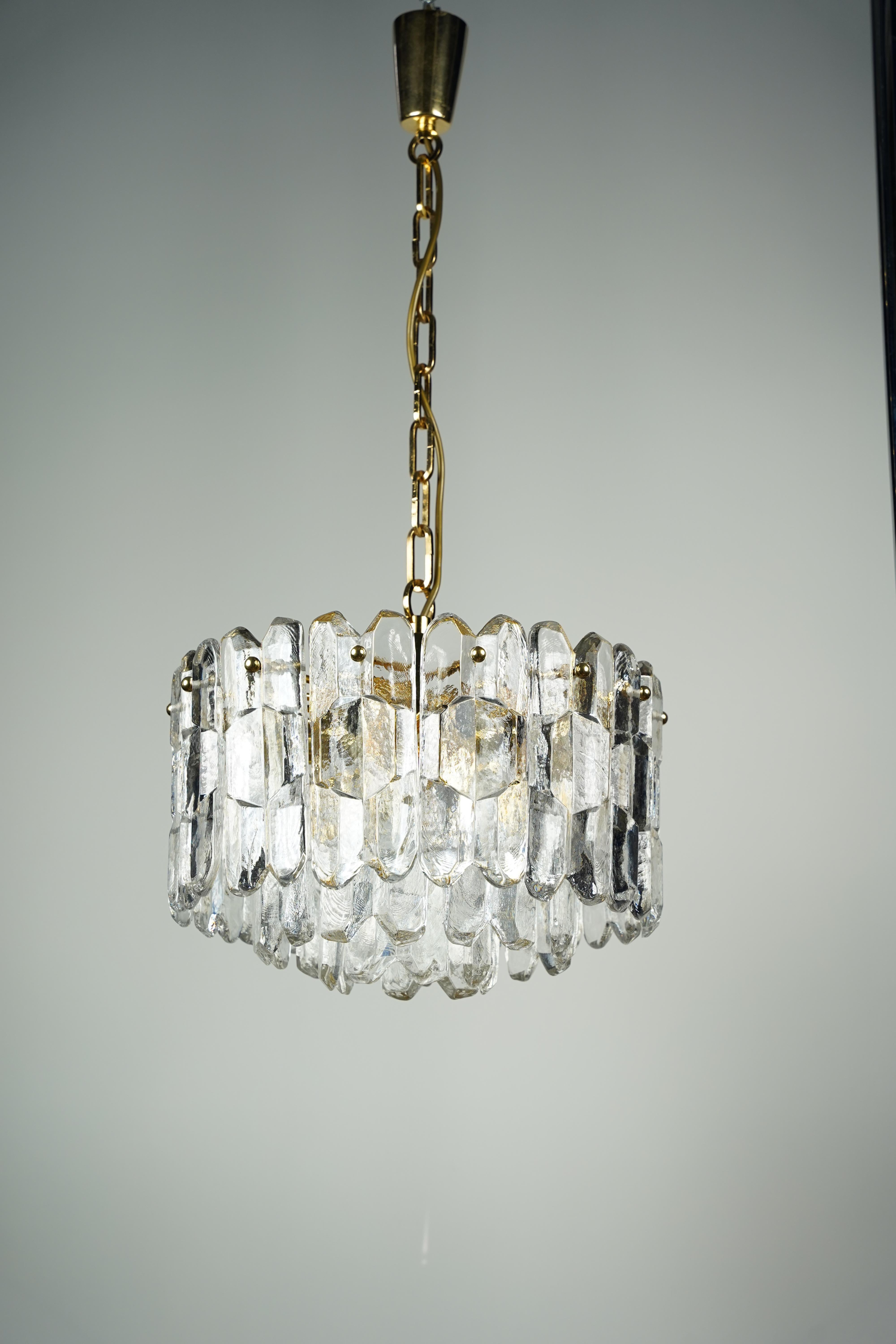 Lámpara de cristal dorado Kalmar Palazzo, 1970, Austria.
Marco dorado en oro que sostiene 26 piezas individuales de cristal grueso prensado,  Siete candelabros que iluminan el cristal lateralmente y uno hacia abajo.
Está en excelentes condiciones,