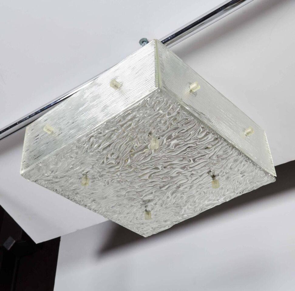 A Kalmar Mid-Century Modern flush mount light with textured glass.
Modernist flush mount light fixture with streamline cubist form. Features multi-textural glass on all sides looking like ice. The fixtures features a floating square ceiling plate