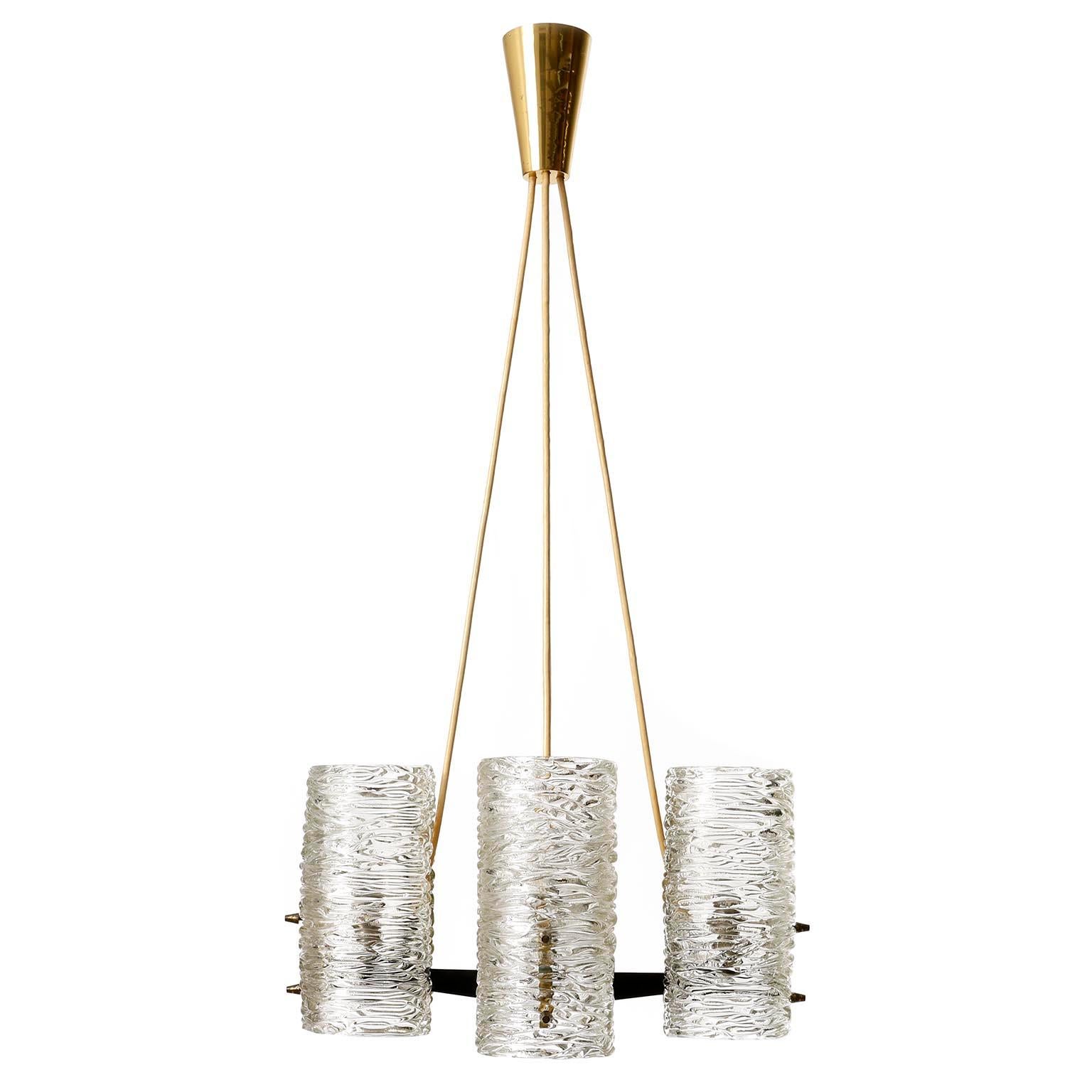 A textured glass and brass pendant light or chandelier by J. T. Kalmar, Austria, manufactured in midcentury, circa 1960 (late 1950s or early 1960s). 
A partly blackened and polished 4-arm brass frame with cylindrical lampshades made of structured