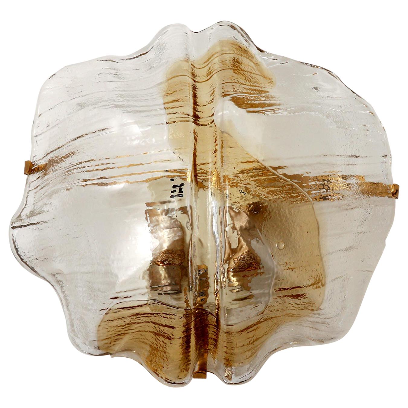 A single wall light fixture by J.T. Kalmar, Austria, manufactured in midcentury, circa 1970 (late 1960s or early 1970s).
An organic shaped clear and amber, golden or bronze toned Murano glass lamp shade is held by a brass bracket on a metal