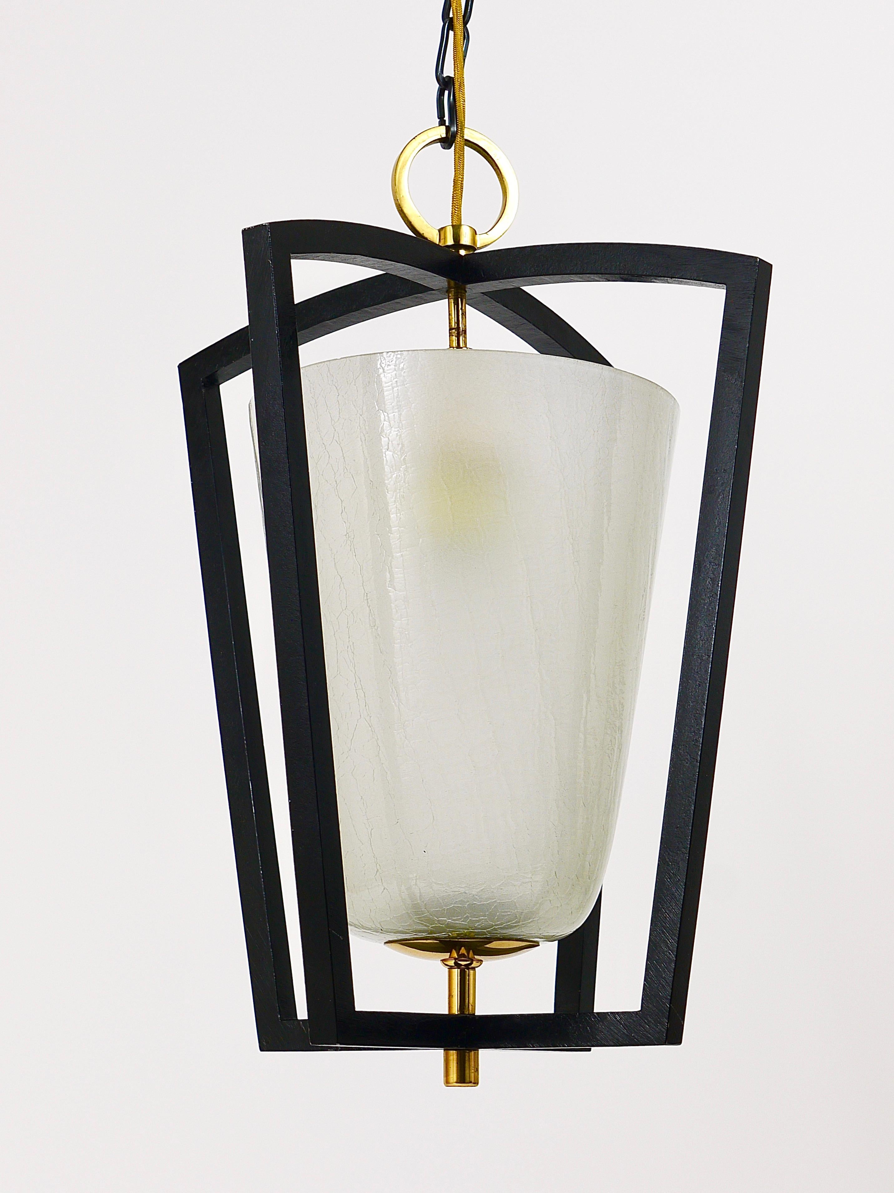 A unusual and beautiful modernist lantern / pendant Light, manufactured by Kalmar Vienna in the early 1950s. An uncommon piece, its frame is made of black iron, it has a satined crackled glass lampshade and an ornamental ring and other nice brass